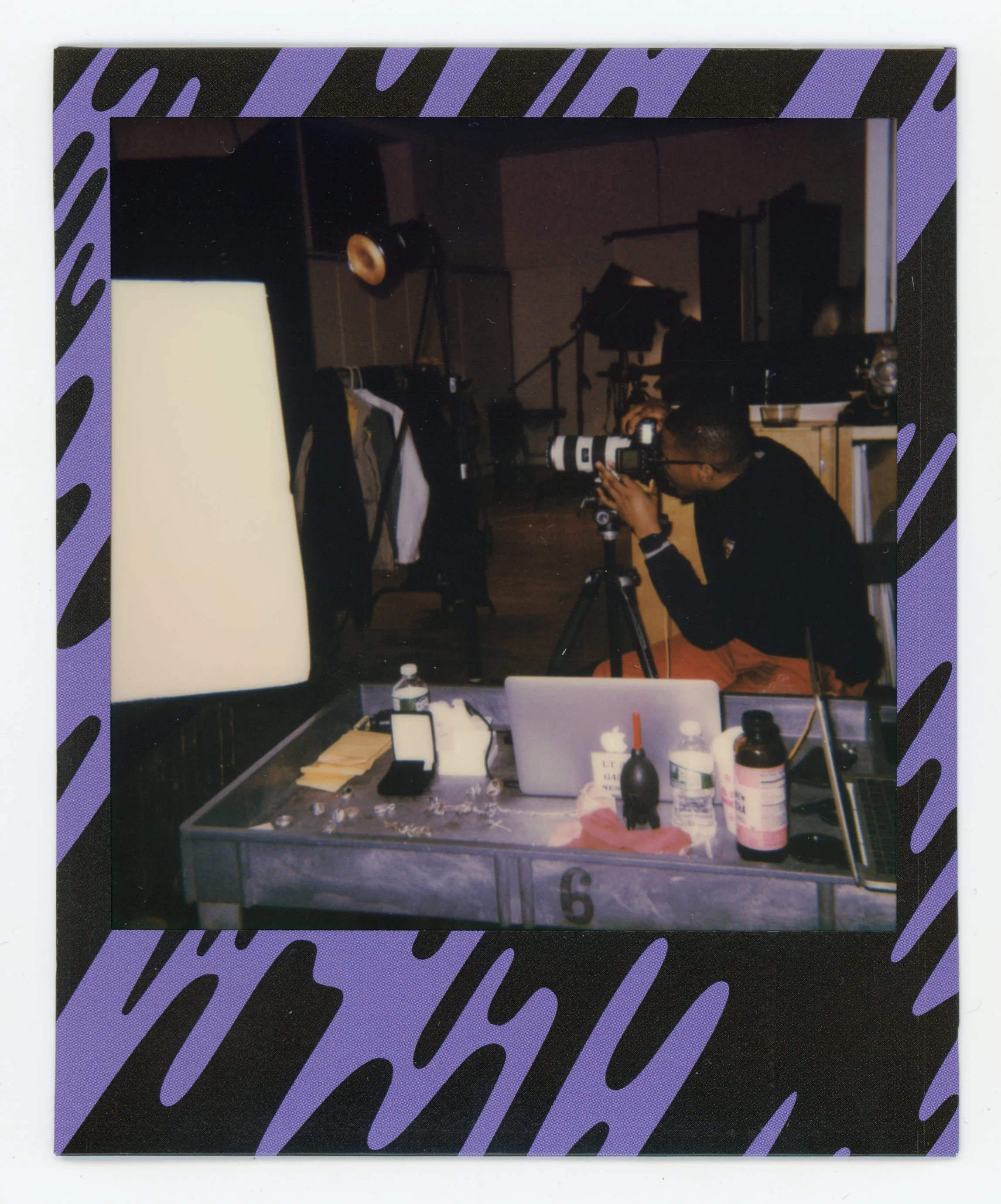 Person using a camera on a tripod in a photography studio, with various equipment and supplies on a table in the foreground.