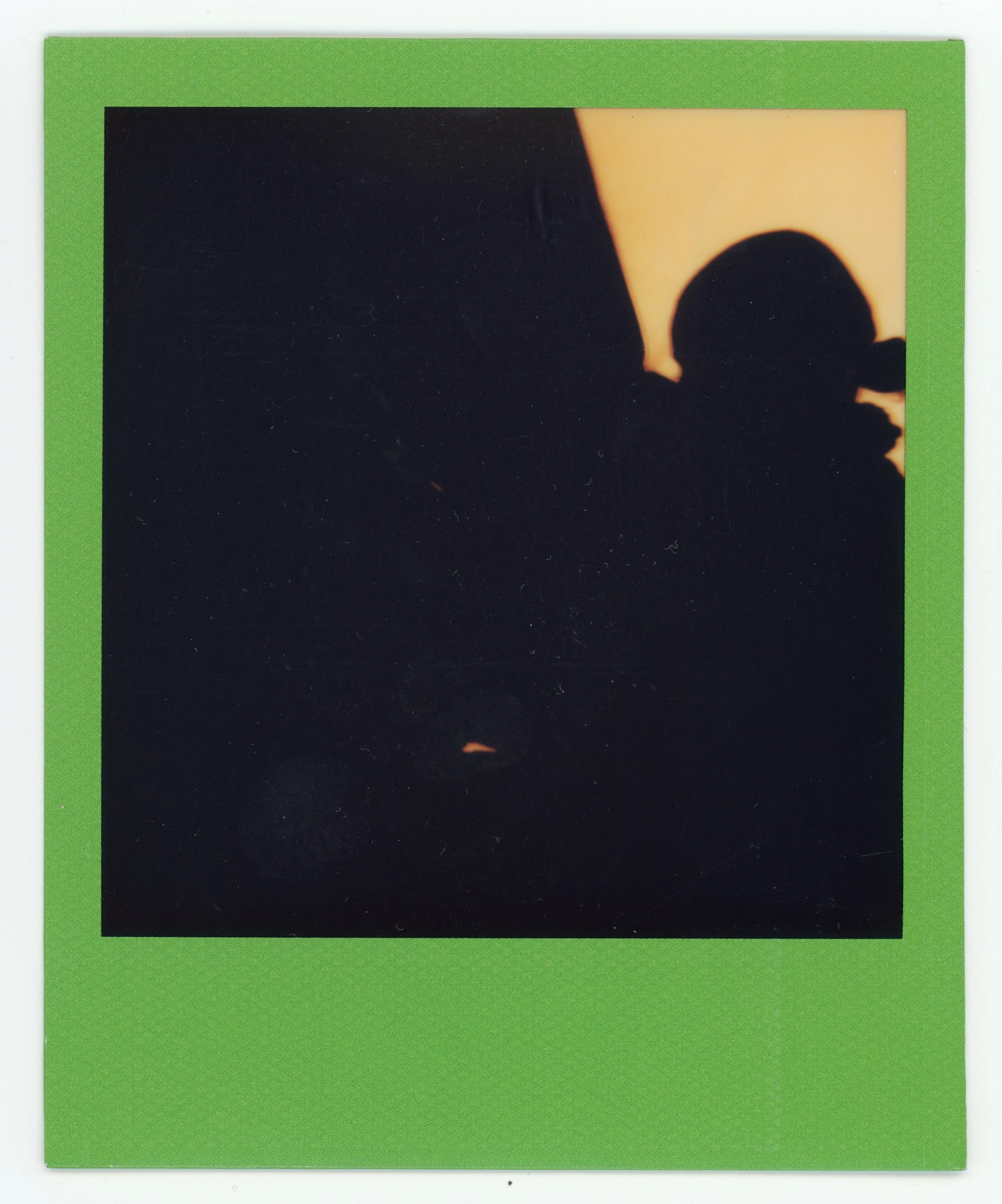 Silhouette of a person wearing a baseball cap against a sunset sky with a green border surrounding the photo.