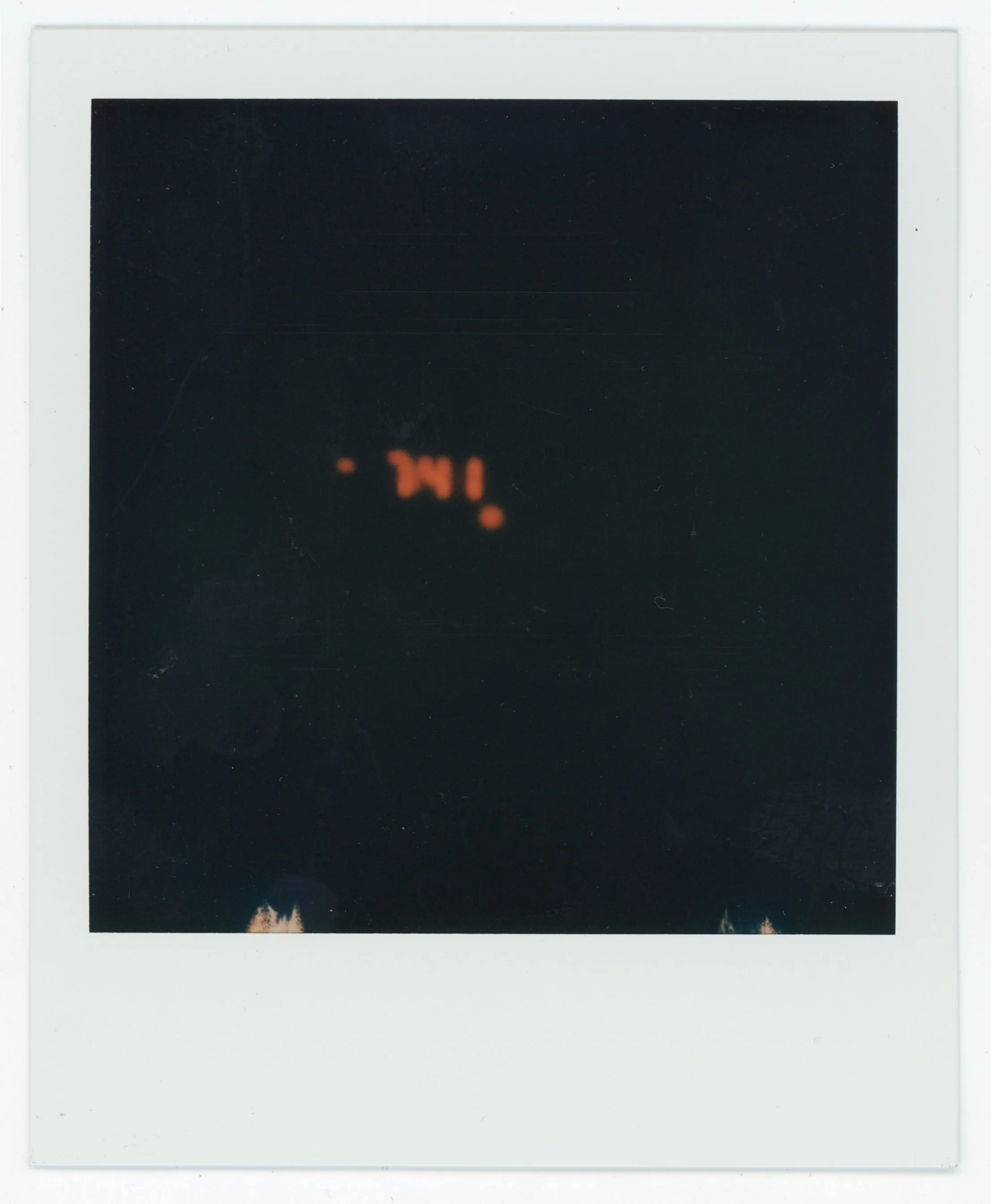 A Polaroid photo with blurred orange lights and the word 'TIME' faintly visible in the center. The photo has a white border and is mostly dark.