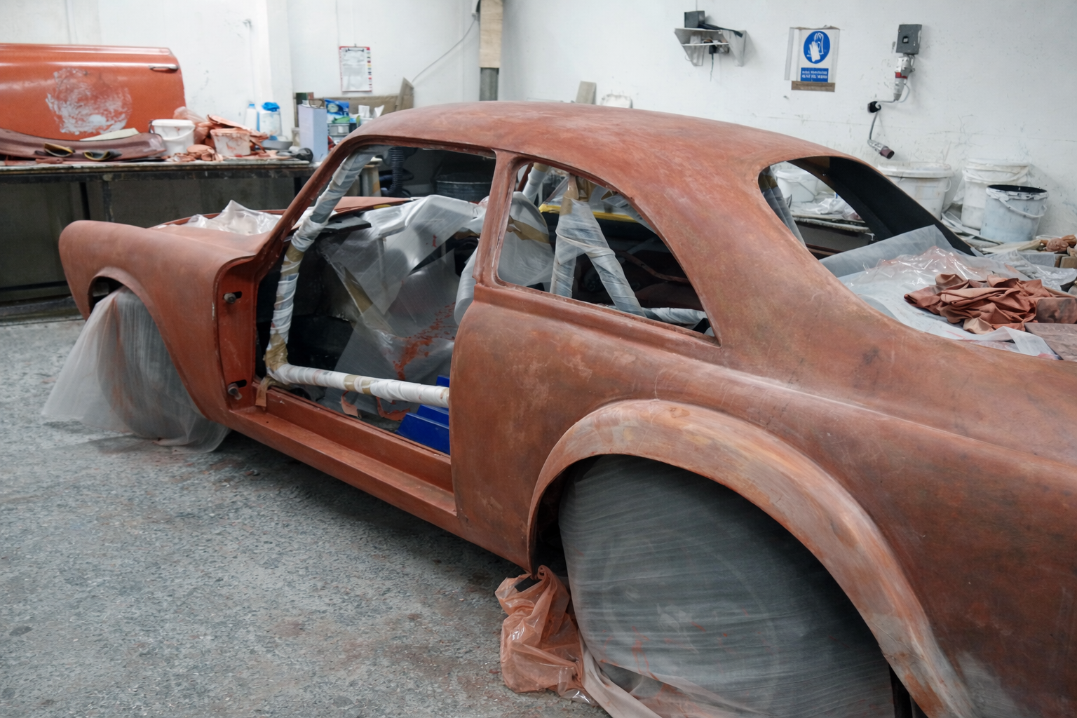 Restoring a vintage red sports car in a workshop, with protection wraps covering the wheels and interior.  Technical Composites .