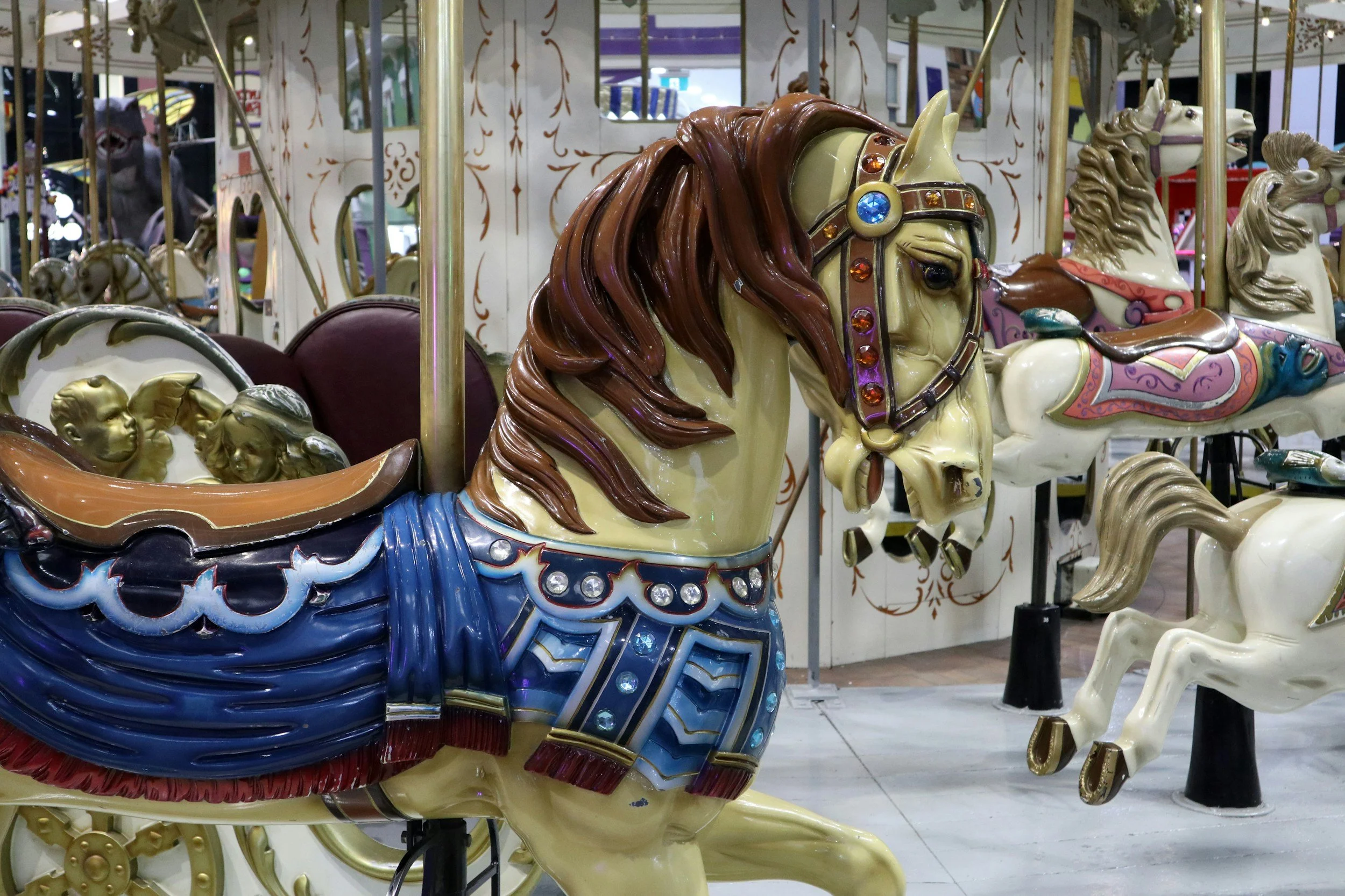 Close-up of a carousel horse with a brown mane and decorative saddle, in an amusement park or fair setting.  Creative and Custom fibreglass and composite solutions. 