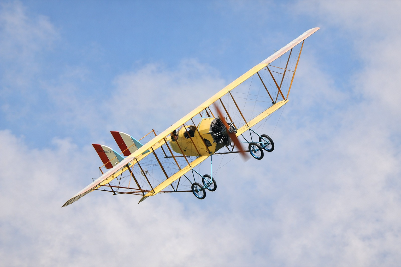 A vintage biplane with yellow wings flying in a partly cloudy sky.  Technical Composites for aerospace.
