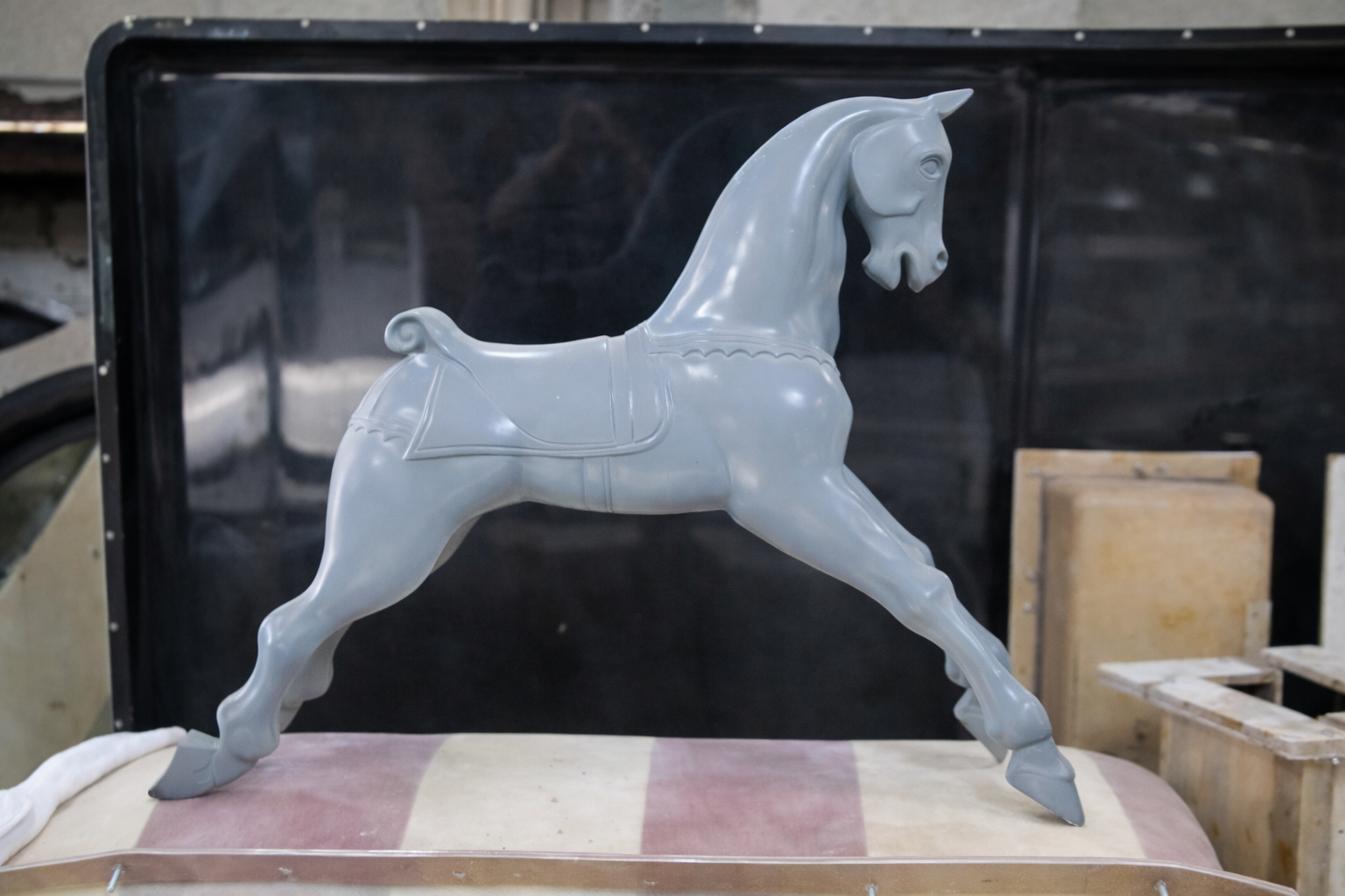 Gray toy rocking horse with saddle, placed on a surface in a workshop or storage area.  Creative and Custom fibreglass and composite solutions. 