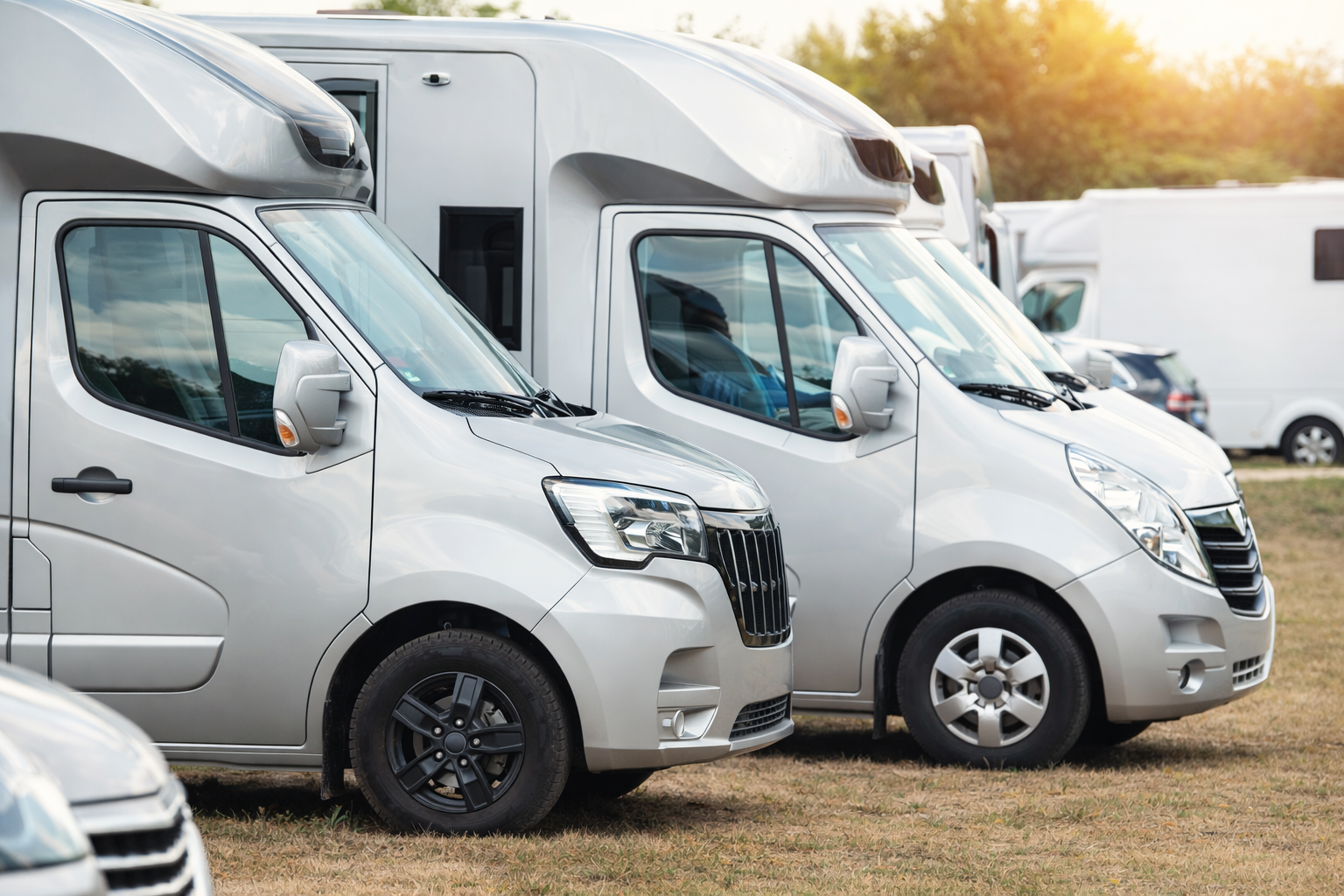 Multiple silver camper vans parked in a row on a grassy field during sunset. Technical Composites.