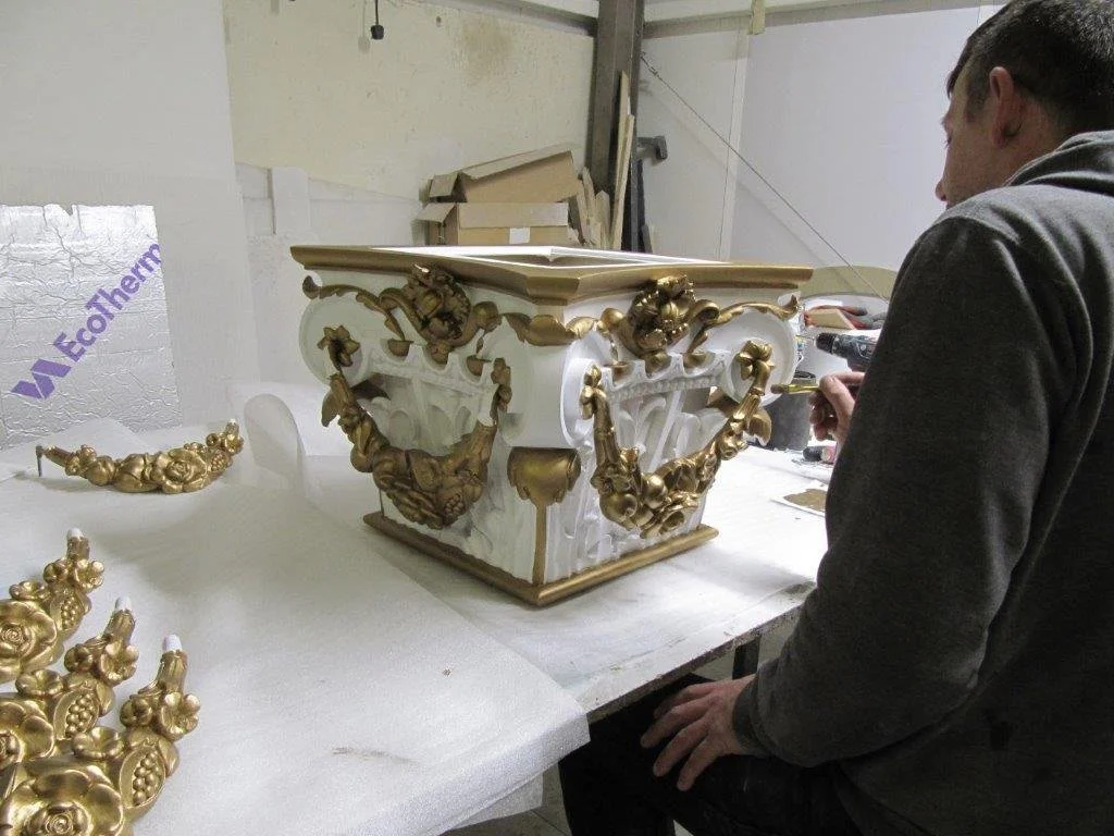 Person working on ornate white and gold decorative furniture with intricate carvings in a workshop.  Creative and Custom fibreglass and composite solutions. 