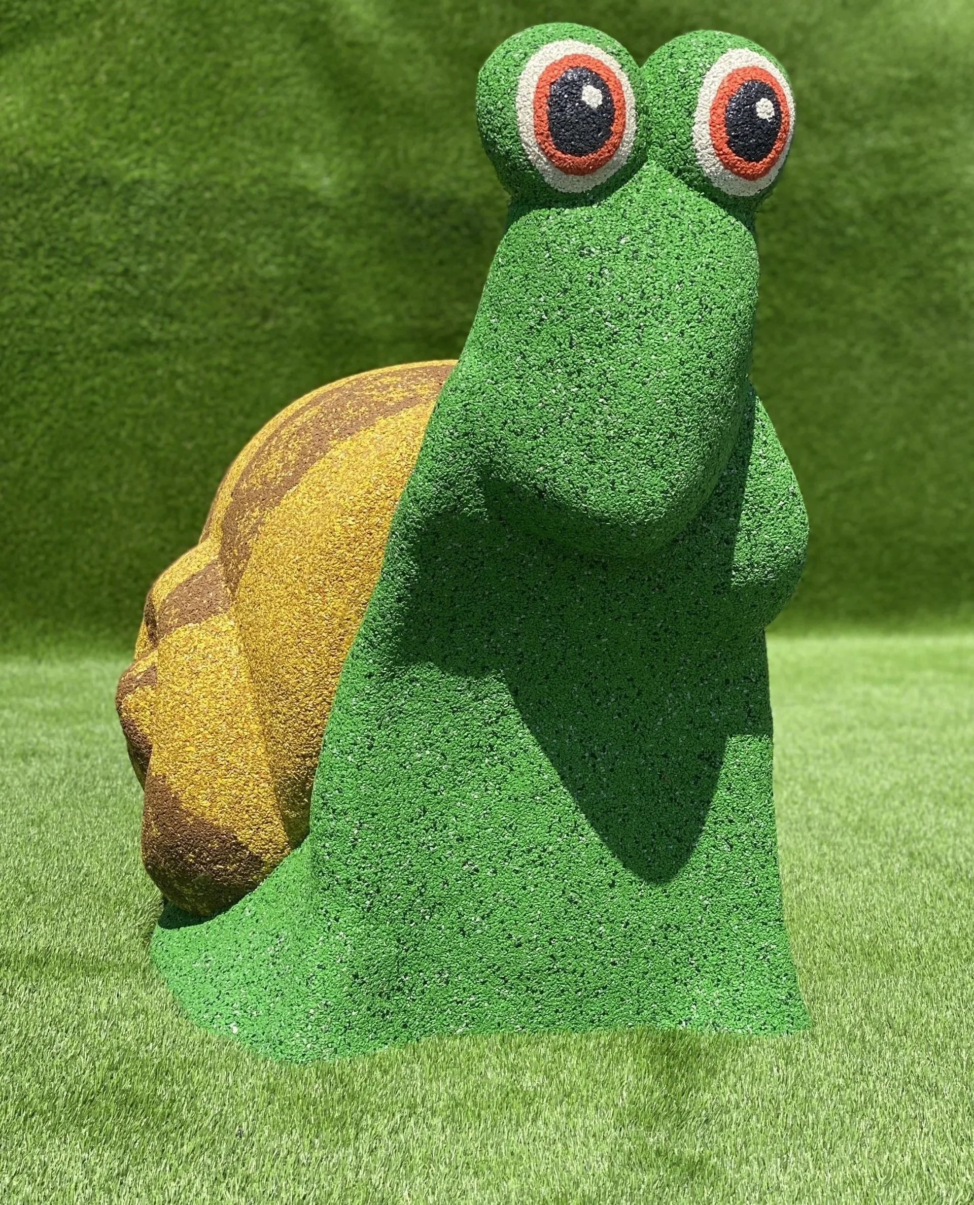 Colorful snail sculpture with green body, yellow shell, and large cartoonish eyes in a grassy outdoor setting for Star Rubber. Creative and Custom fibreglass and composite solutions.