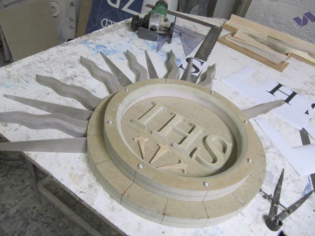 A workshop table with a partially assembled sun-shaped wooden mould, surrounded by a circular frame, and materials and tools for woodworking.  Creative and Custom fibreglass and composite solutions. 