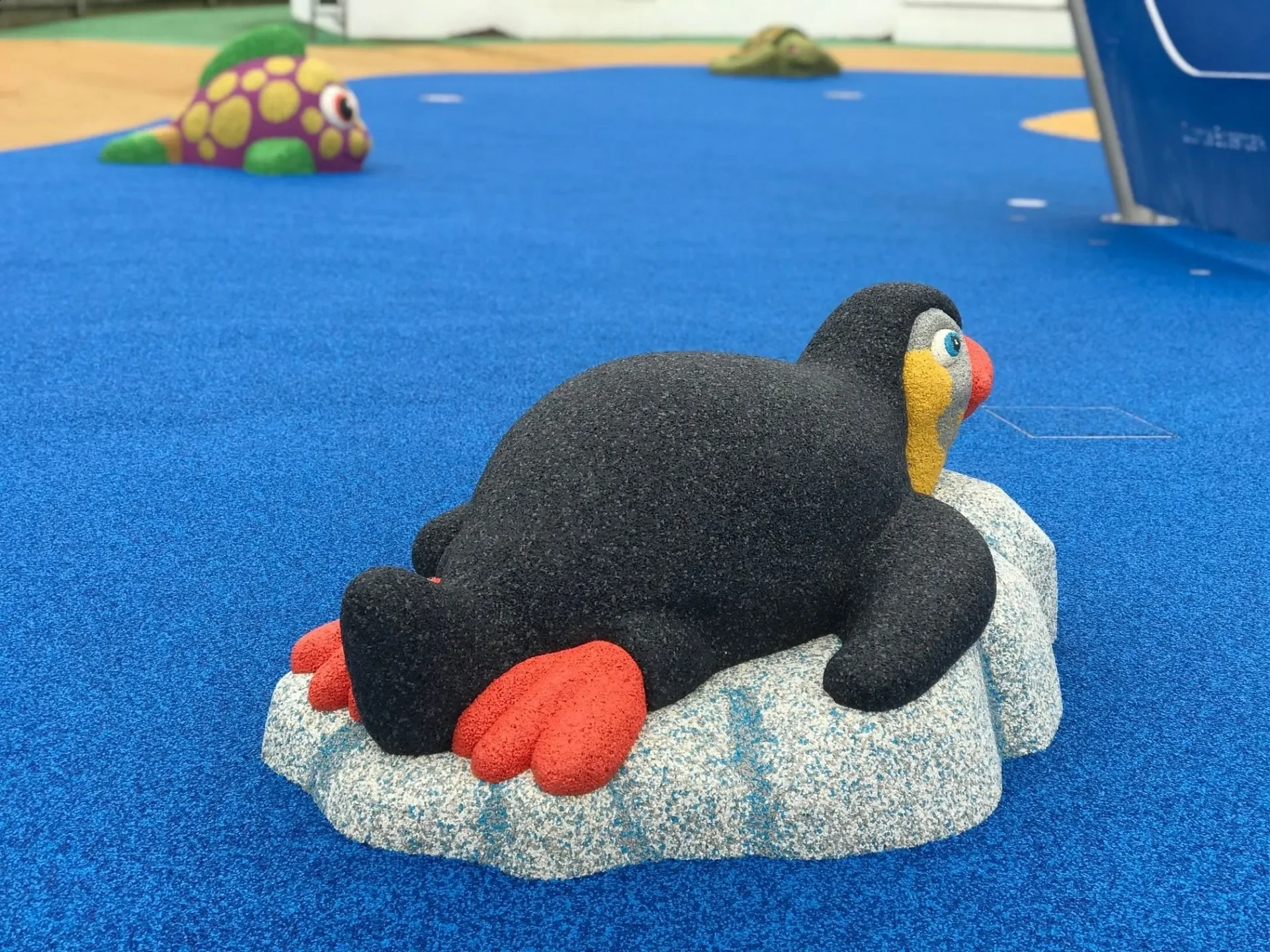 Colorful cartoon animal statues, including a black bird with orange feet and multicolored face, on a blue surface at a playground for Star Rubber. Creative and Custom fibreglass and composite solutions.