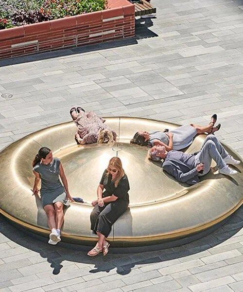People relaxing on a large, circular, golden seating structure outdoors on a paved area. Sculpture. Art.  Creative and Custom fibreglass and composite solutions. 