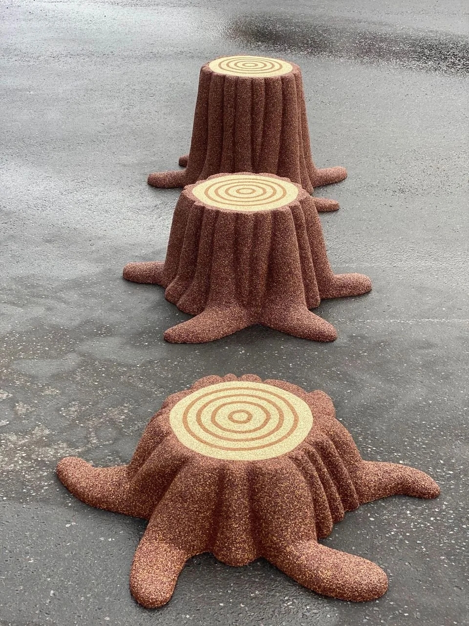 Two tree stump-shaped seats with swirl pattern tops, placed on an asphalt surface, one in front of the other for Star Rubber. Creative and Custom fibreglass and composite solutions.