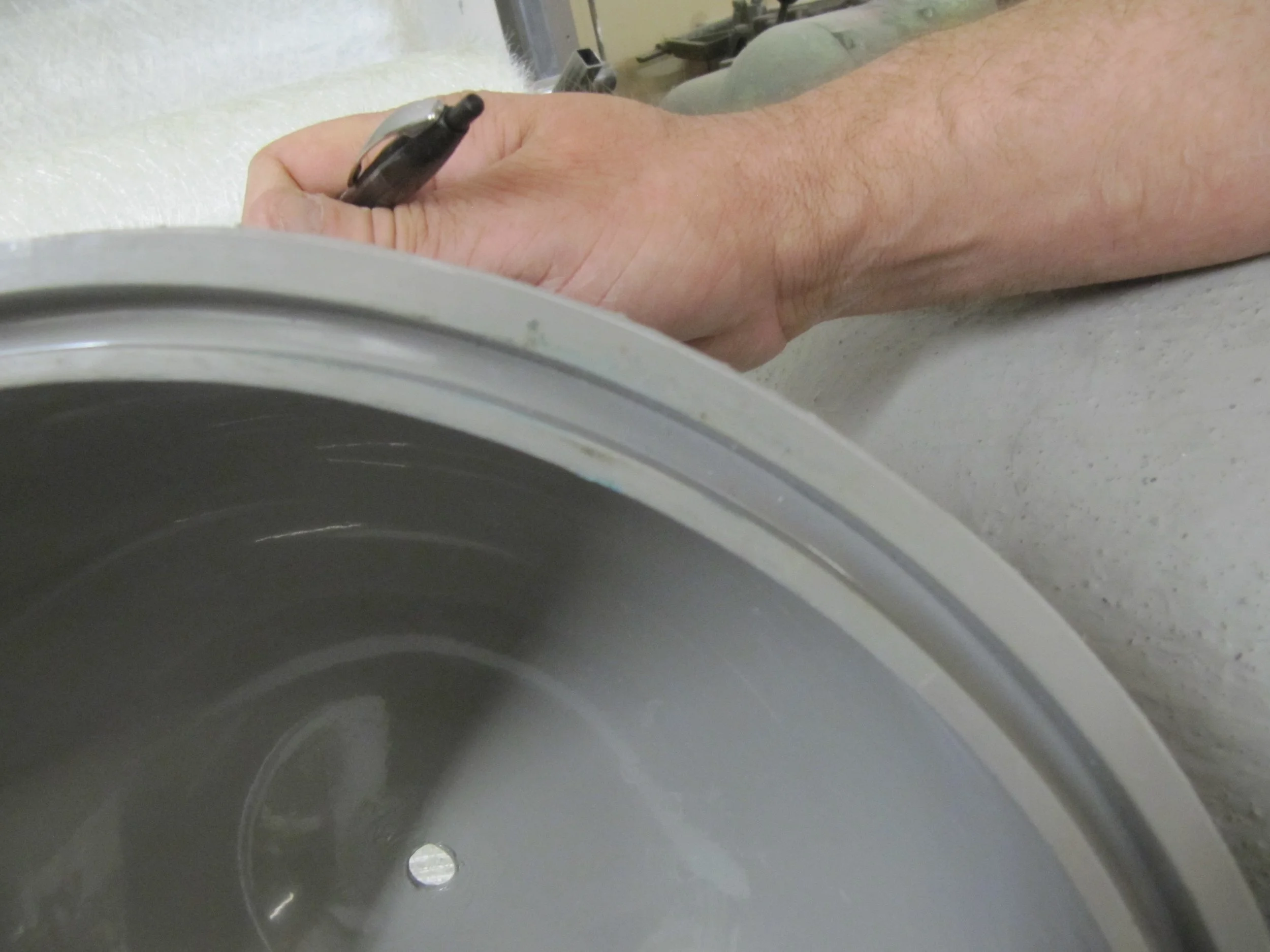 Close-up of a person's hand holding a black pen, resting on the rim of a fibreglass component. Creative and Custom fibreglass and composite solutions.