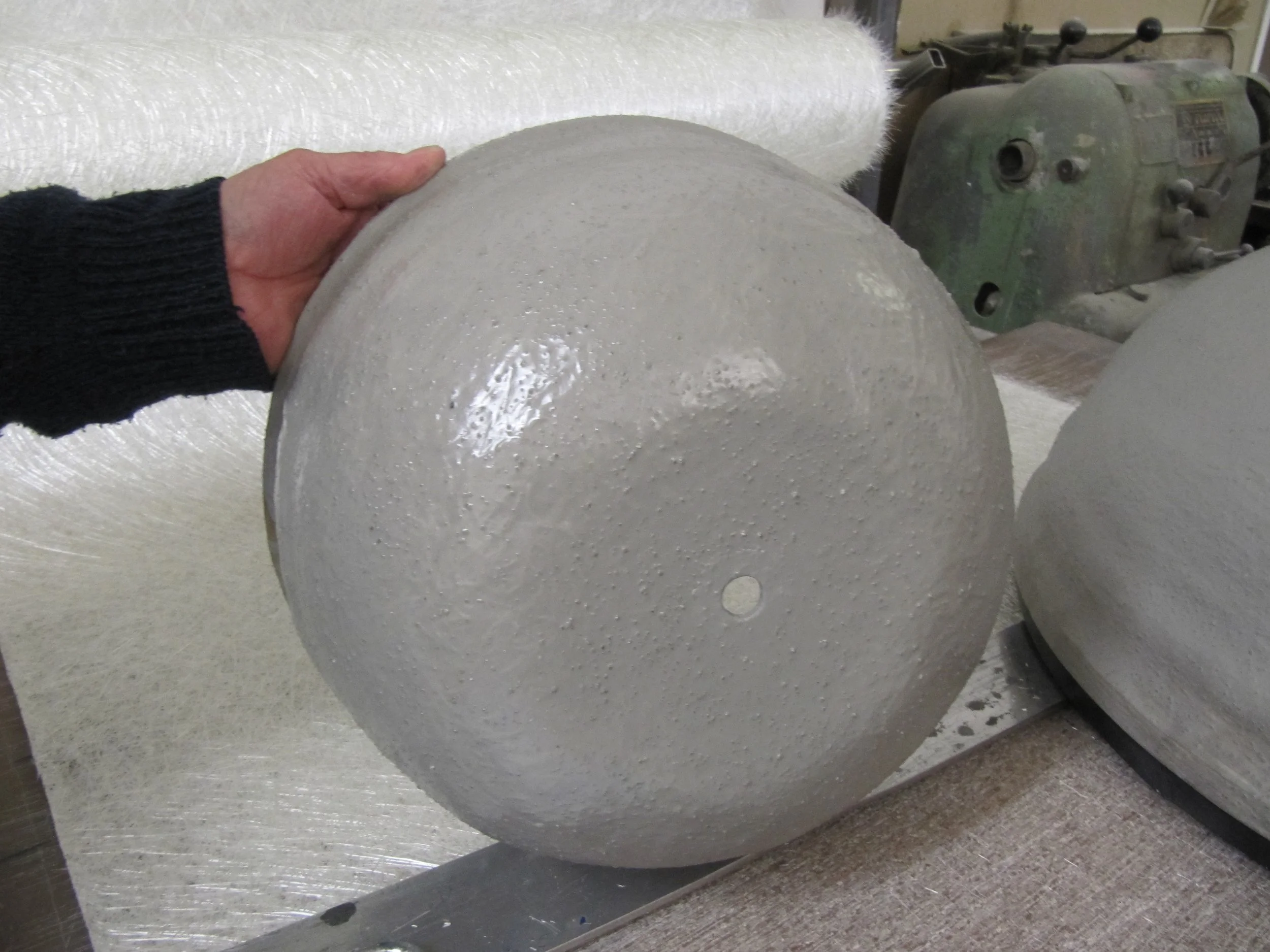 Person holding a spherical fibreglass object with a textured, painted surface, in a workshop setting. Creative and Custom fibreglass and composite solutions.