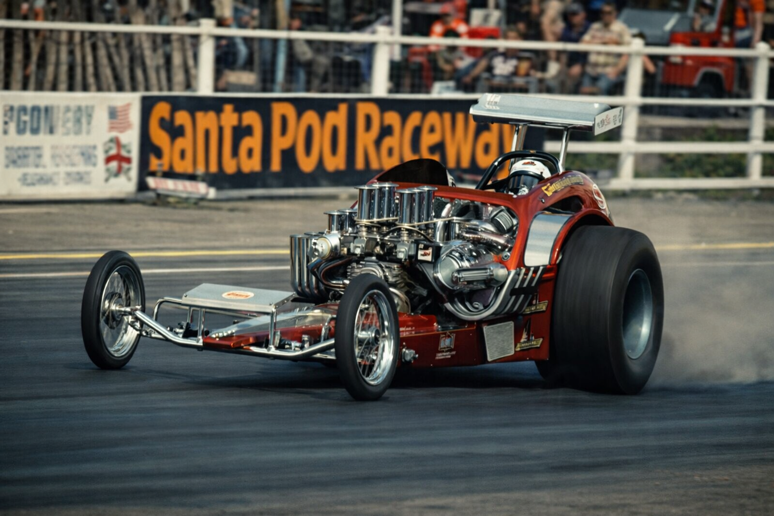 A drag racing car on the track at Santa Pod Raceway during a race, with spectators in the background.