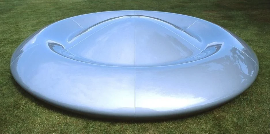 A shiny, modern, silver, saucer-shaped car set on grass. Sculpture. Art. Chatsworth. Creative and Custom fibreglass and composite solutions. 