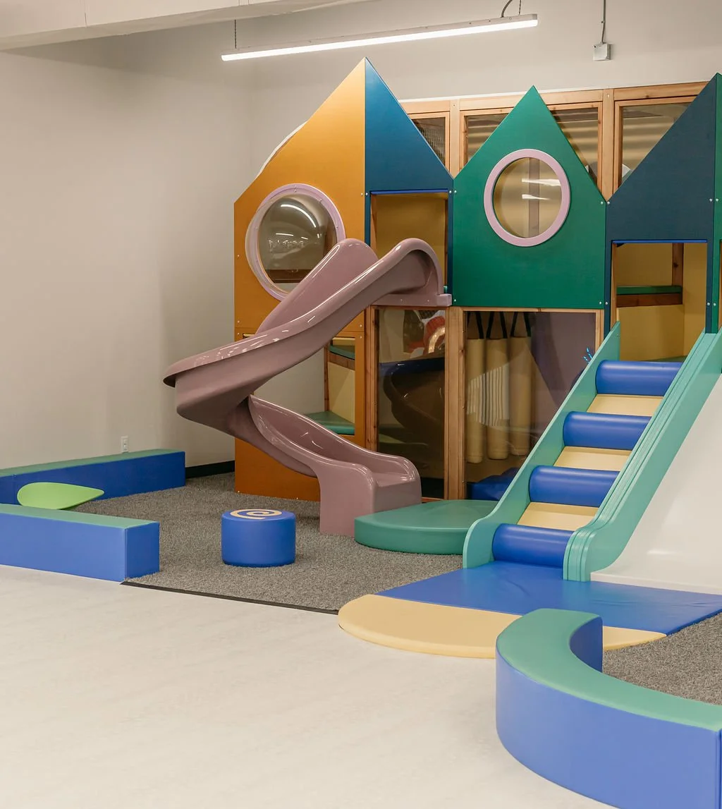 Colourful indoor children's play structure with fibreglass slides, tunnels, and climbing areas in a room with beige walls and ceiling lights. Creative and Custom fibreglass and composite solutions.
