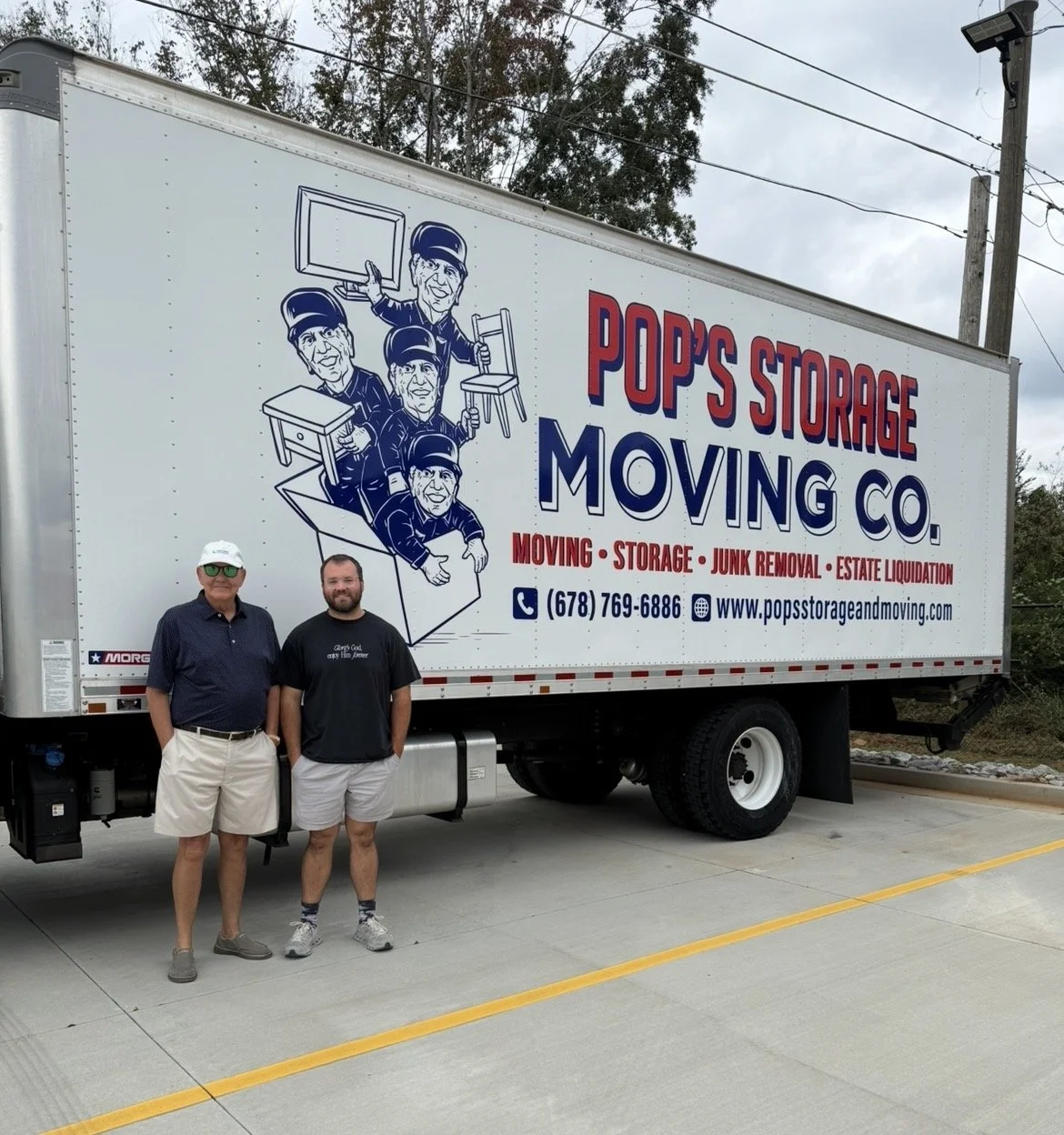 A large moving truck with the logo and branding for Pop's Storage Moving Co., featuring cartoon illustrations of five men with boxes. Two men are standing in front of the truck, one wearing a white cap and dark shirt, the other in a black shirt and shorts.