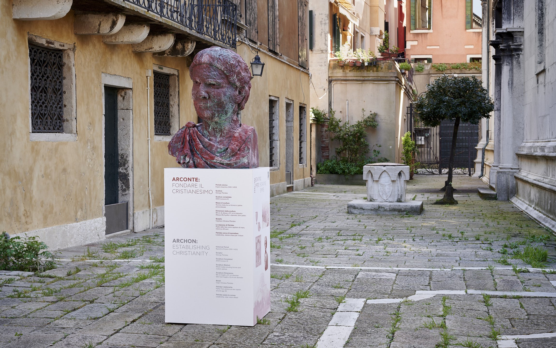A bust sculpture of a woman on display in a rustic outdoor courtyard, with informational signage in front of it.