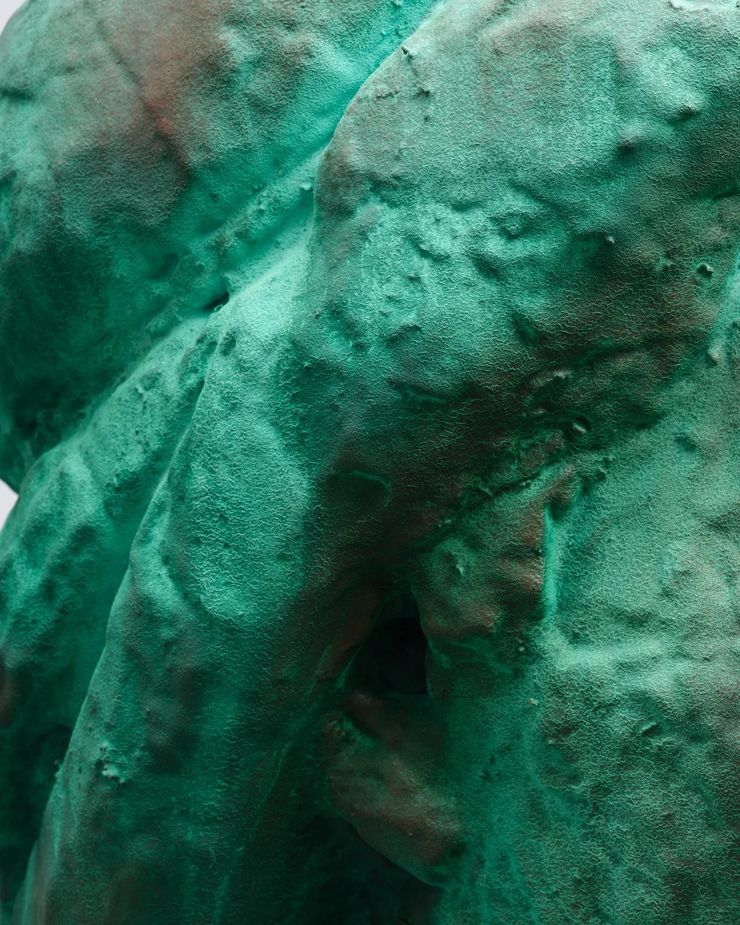 Close-up of a weathered, greenish-blue metal sculpture of a person's face.