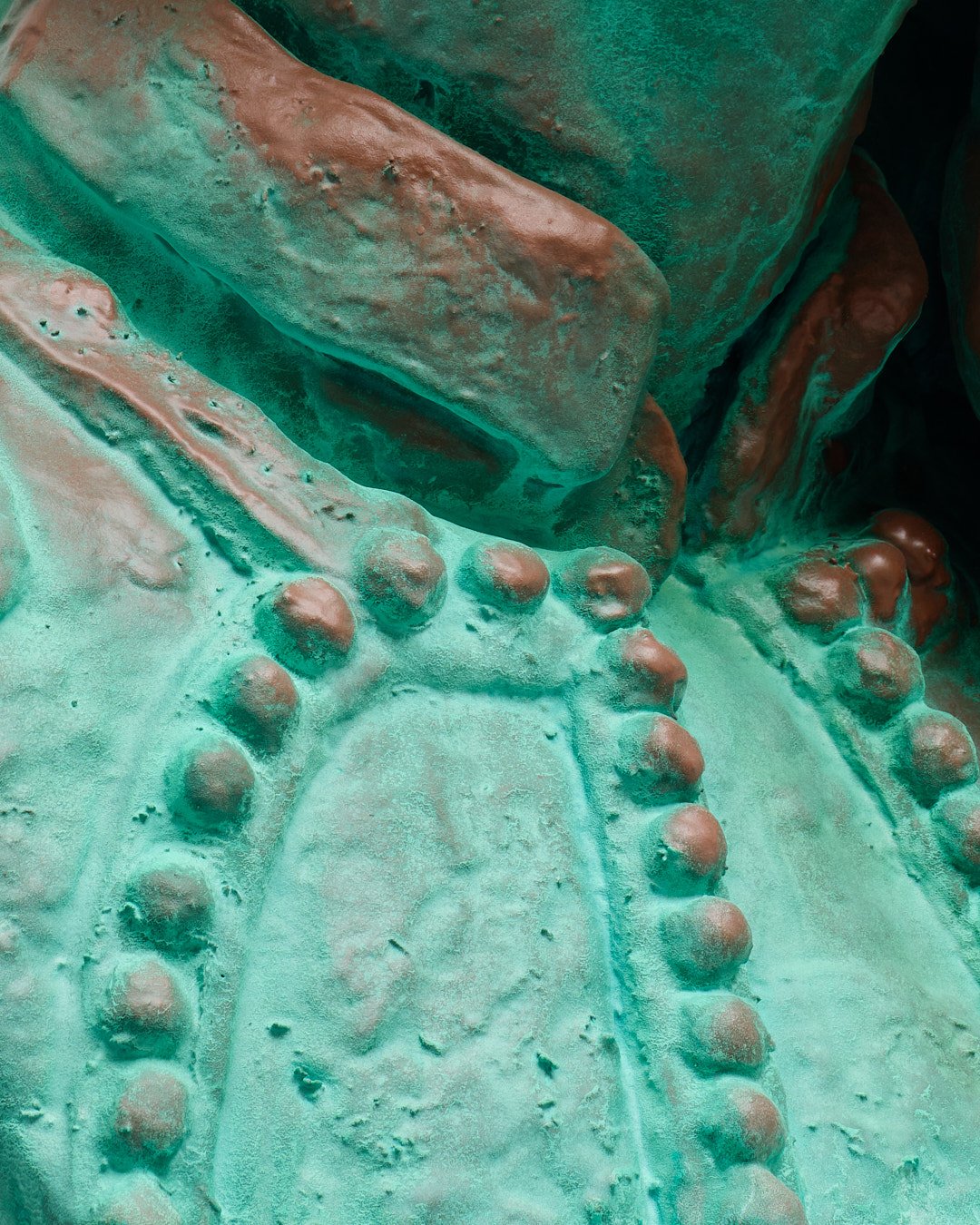 Close-up of a bronze or copper sculpture featuring rounded bumps and textured surfaces in green patina.