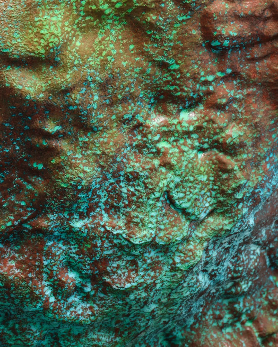 Close-up photo of a textured surface covered in bright green and red patches, resembling a patina or corrosion on metal.