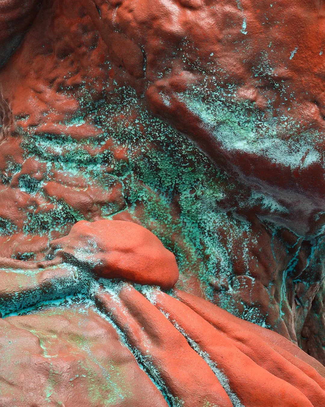 Close-up of a rocky surface with rust-colored tones and turquoise mineral deposits.