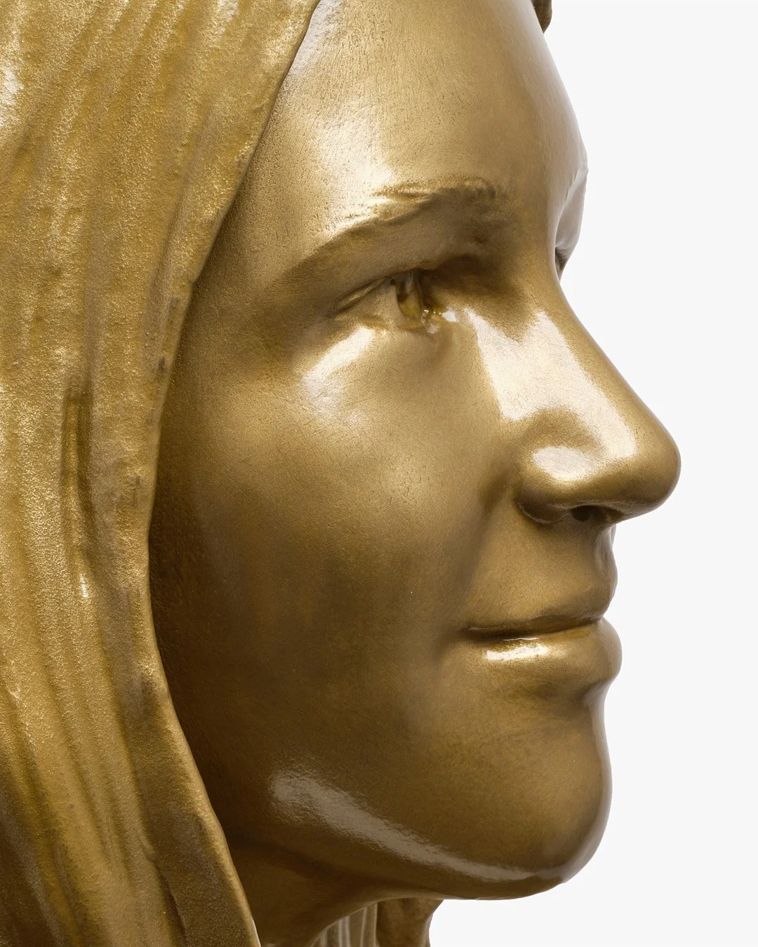 Close-up of a gold-colored statue of Jesus Christ, showing his face in profile with a gentle expression.