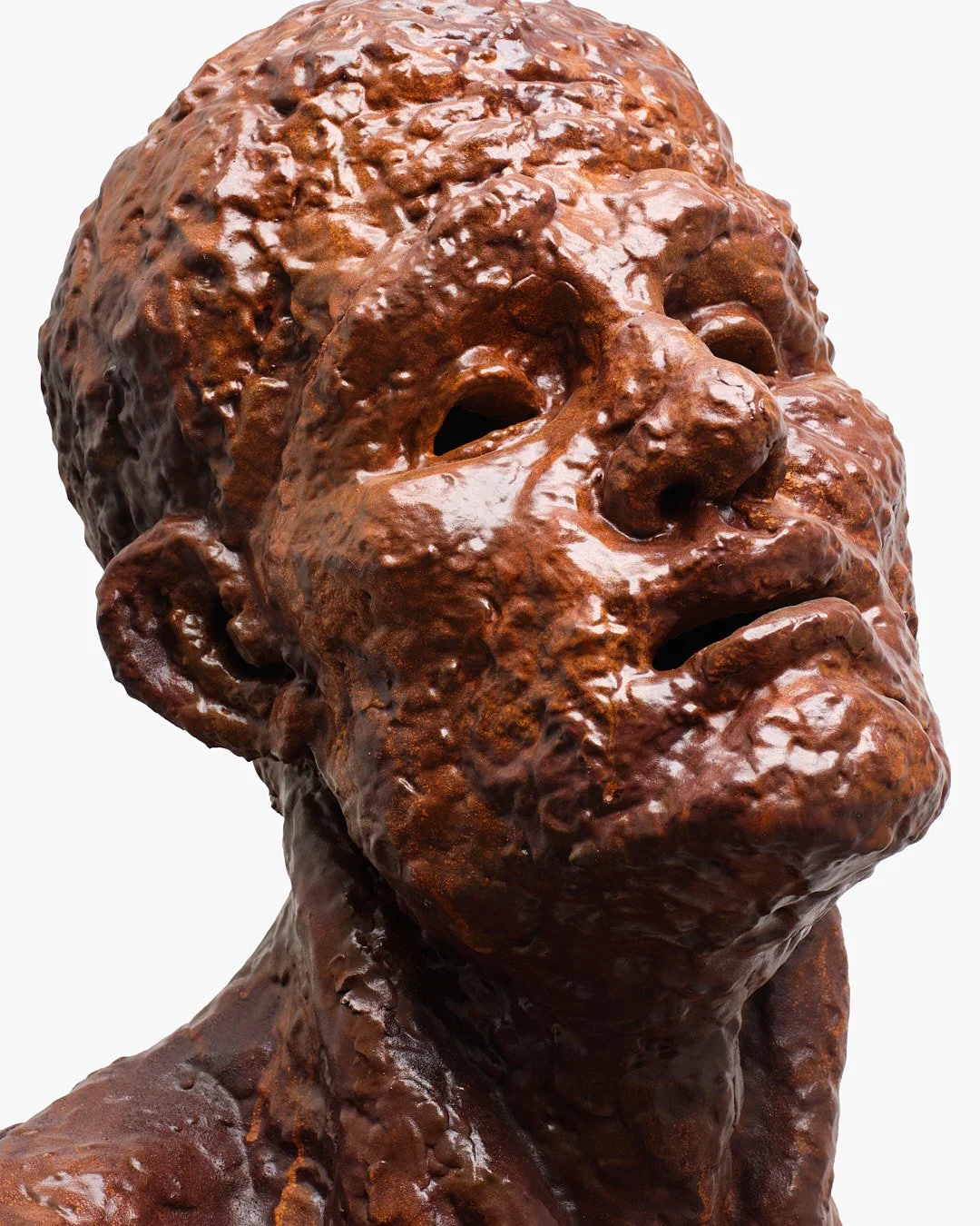 A sculpture of a human head and shoulder, made with a rough, textured, chocolate-like material, giving it a glossy, uneven surface.