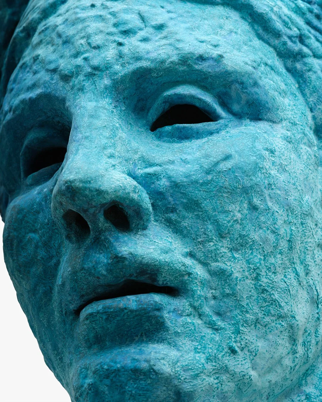Close-up of a blue-green sculpture of a face, showing detailed facial features including closed eyes, nose, and mouth.