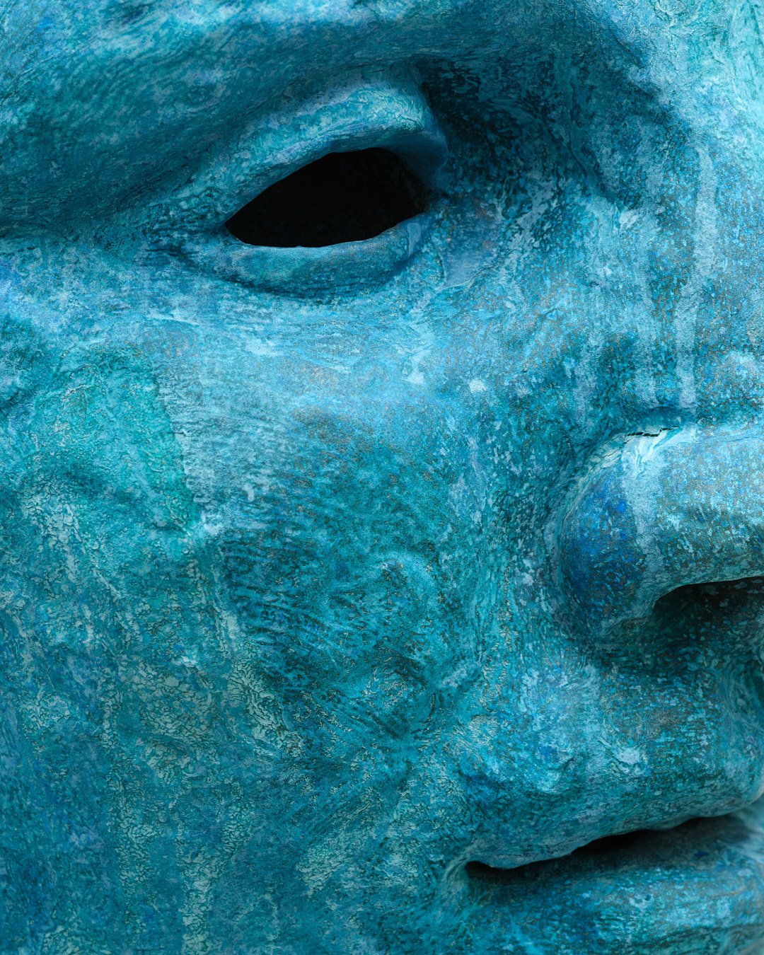 Close-up of a blue abstract sculpture resembling a human face, focusing on the eye and part of the nose and lips.