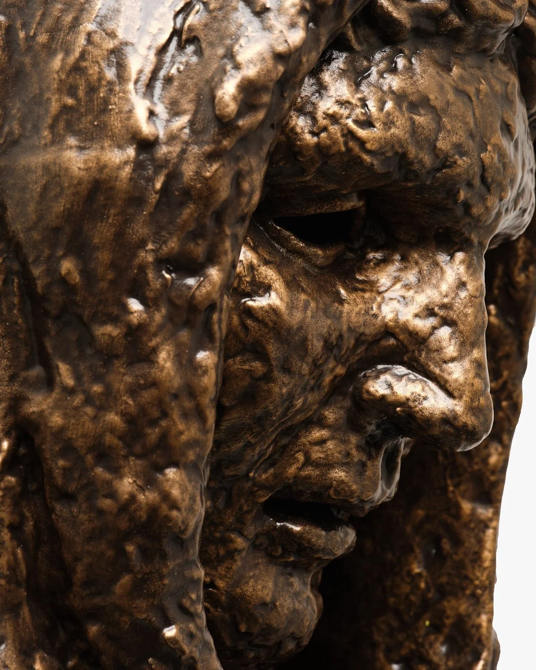 Close-up of a textured bronze sculpture of a human face showing detailed facial features.