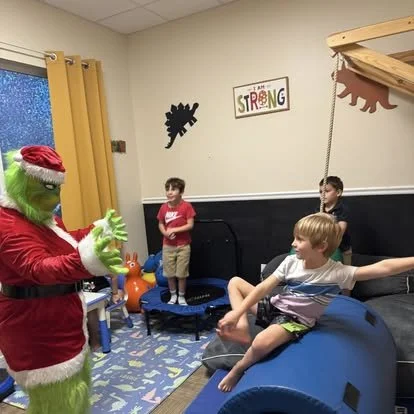 Children playing with a person dressed as the Grinch in a decorated room.