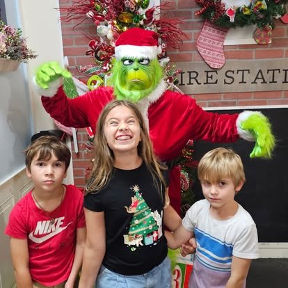 Four children with a person dressed as the Grinch in front of a decorated Christmas fireplace and tree.