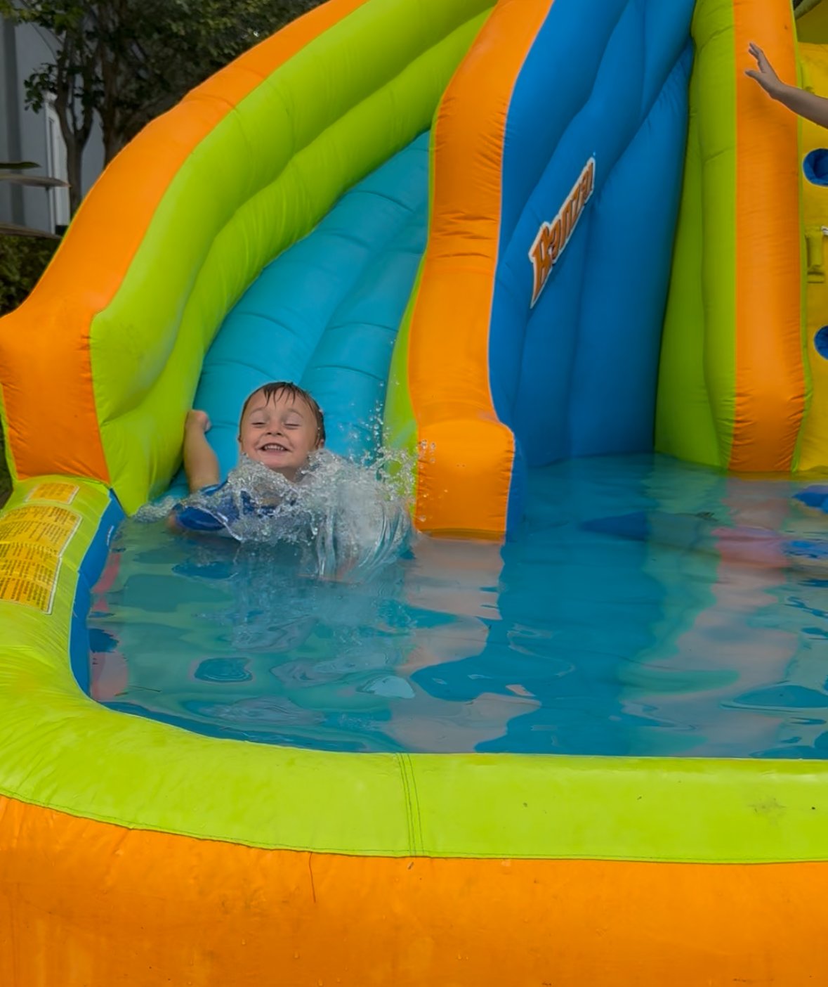 Young boy smiling and enjoying himself on an inflatable water slide.