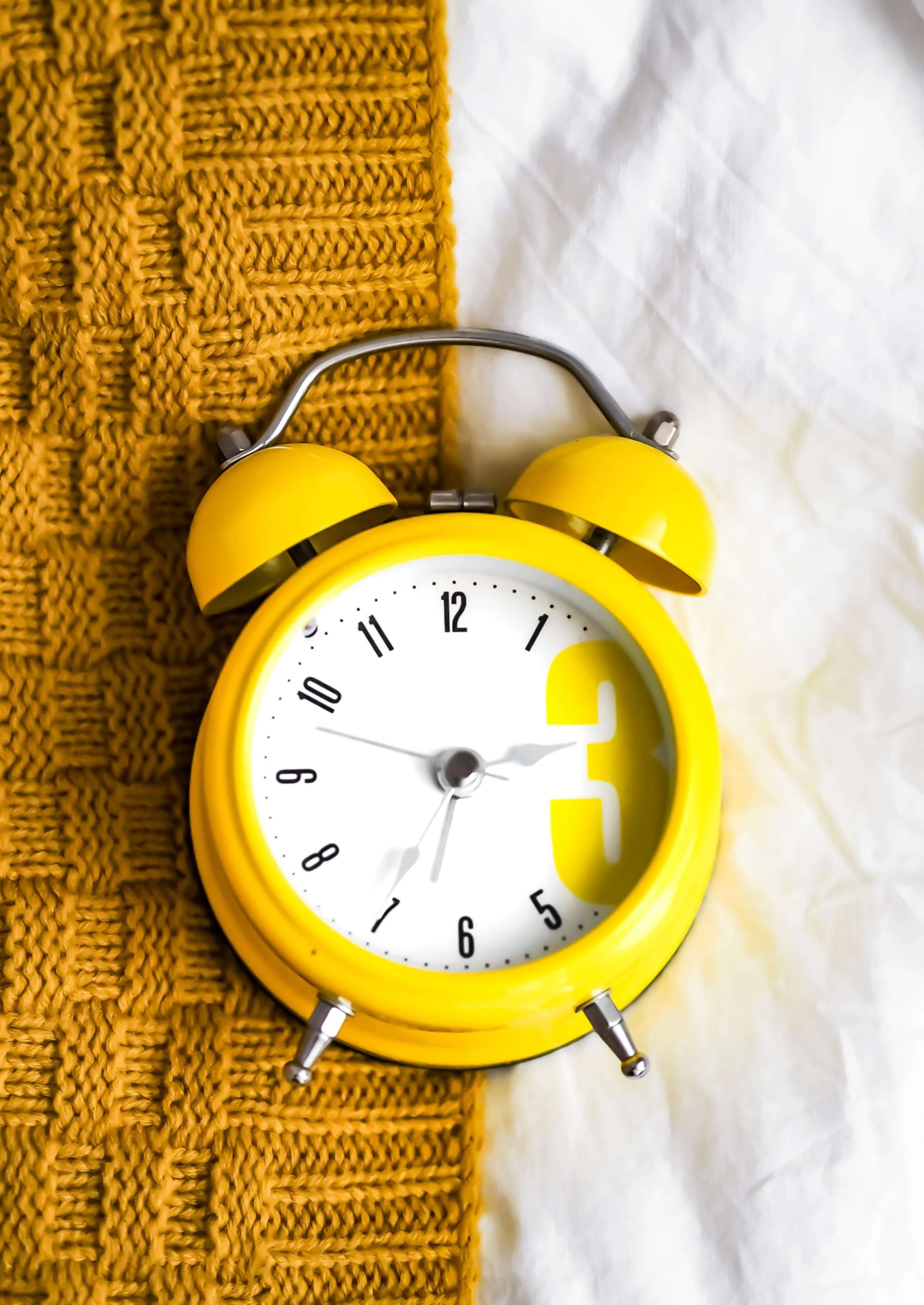Yellow vintage-look alarm clock lying on bed