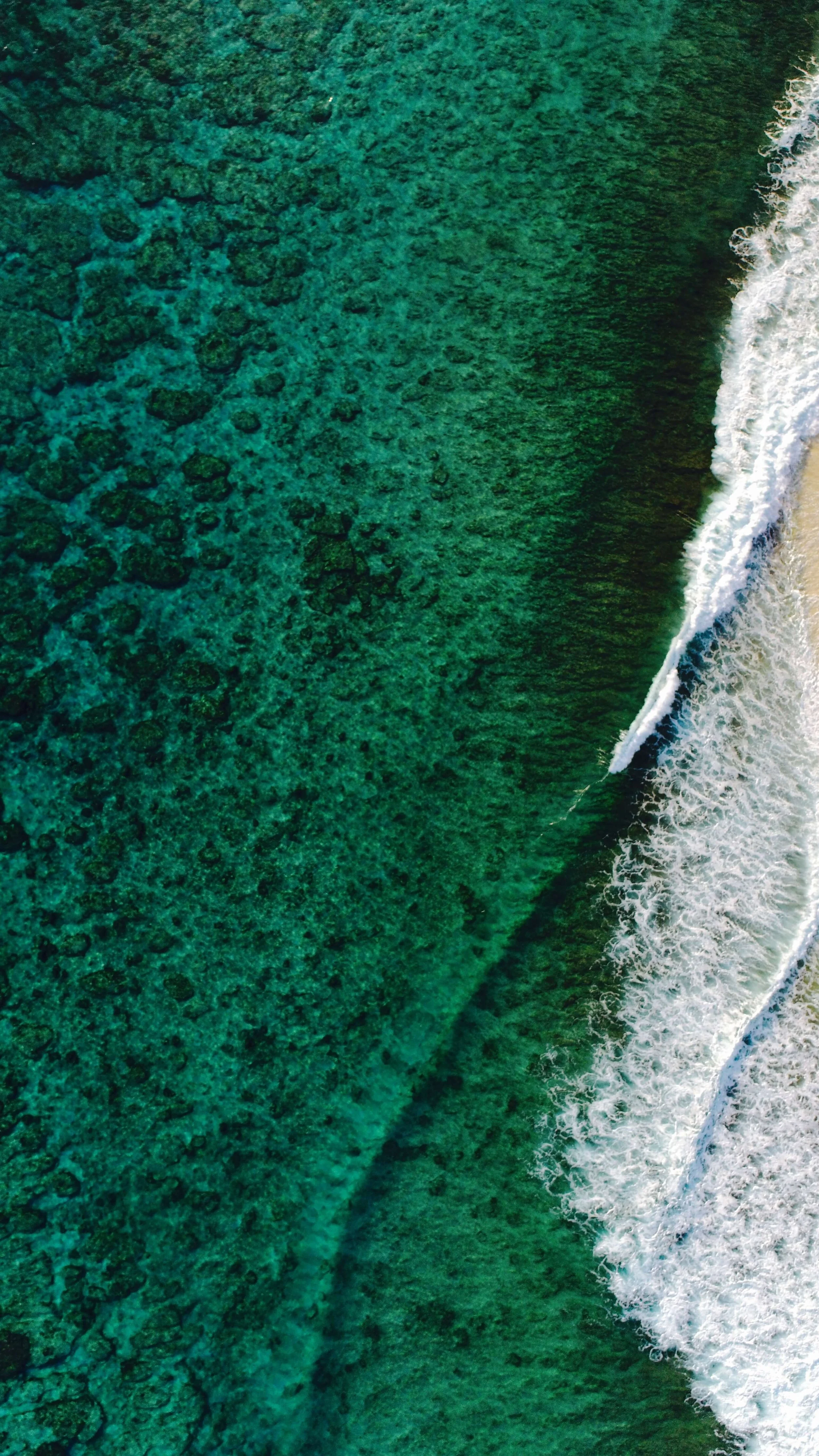 Aerial shot of turquoise sea with small waves on shore