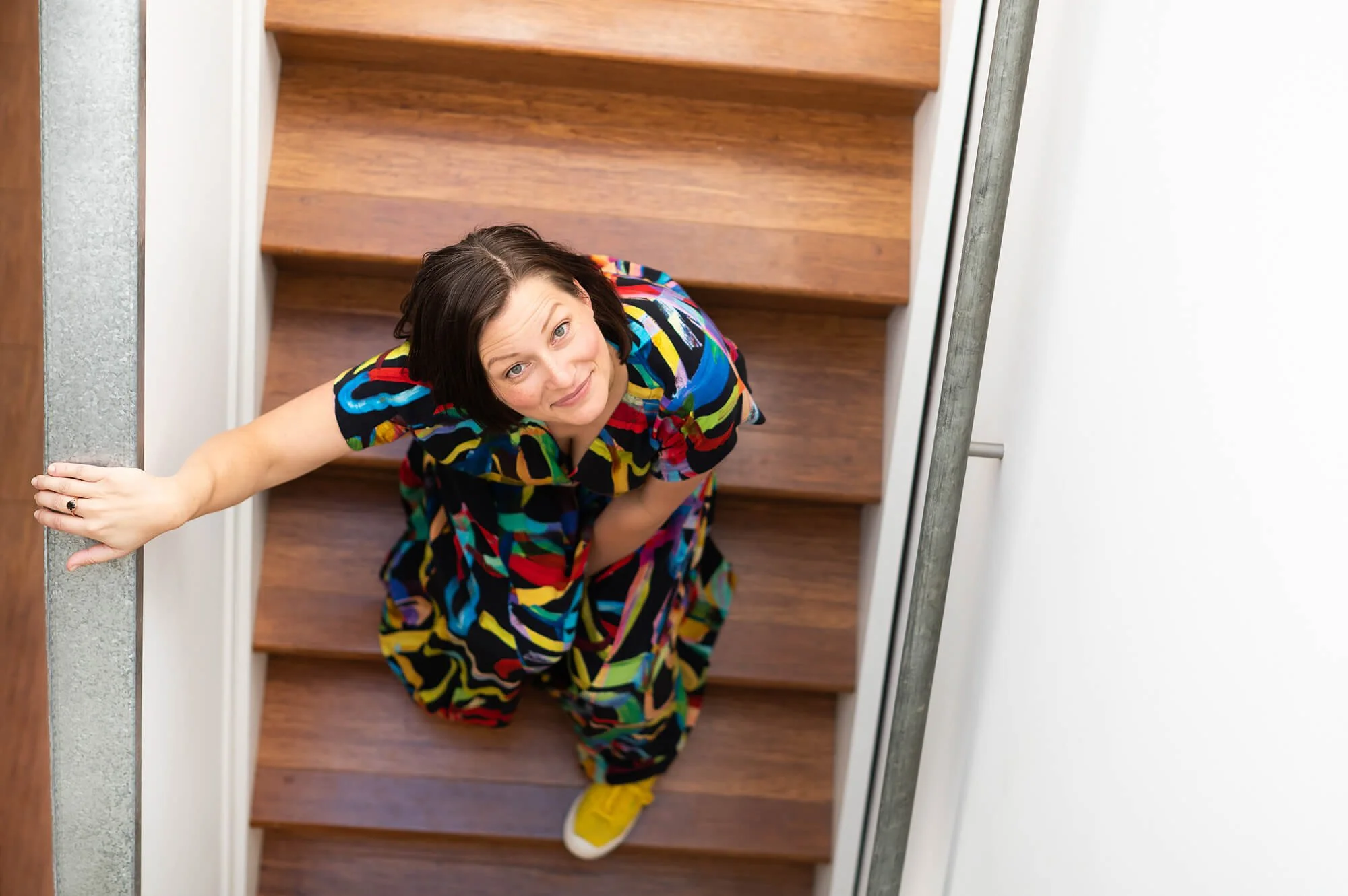 Meditation teacher sitting on stairs, looking up at camera, smiling.