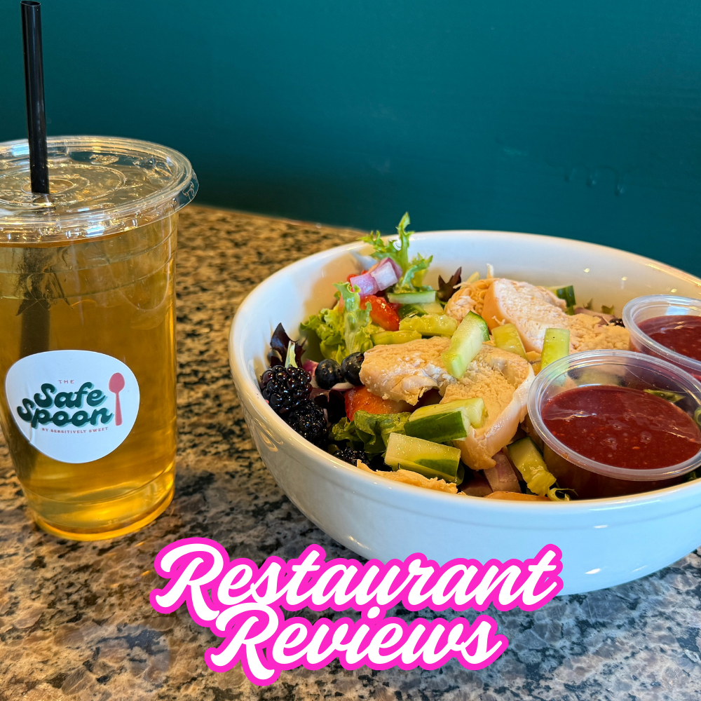 A bowl of salad with mixed greens, chicken, cucumbers, and berries, two cups of ketchup, and a tall iced tea drink on a granite table with a teal wall in the background. The text 'Restaurant Reviews' is overlaid in pink and white.