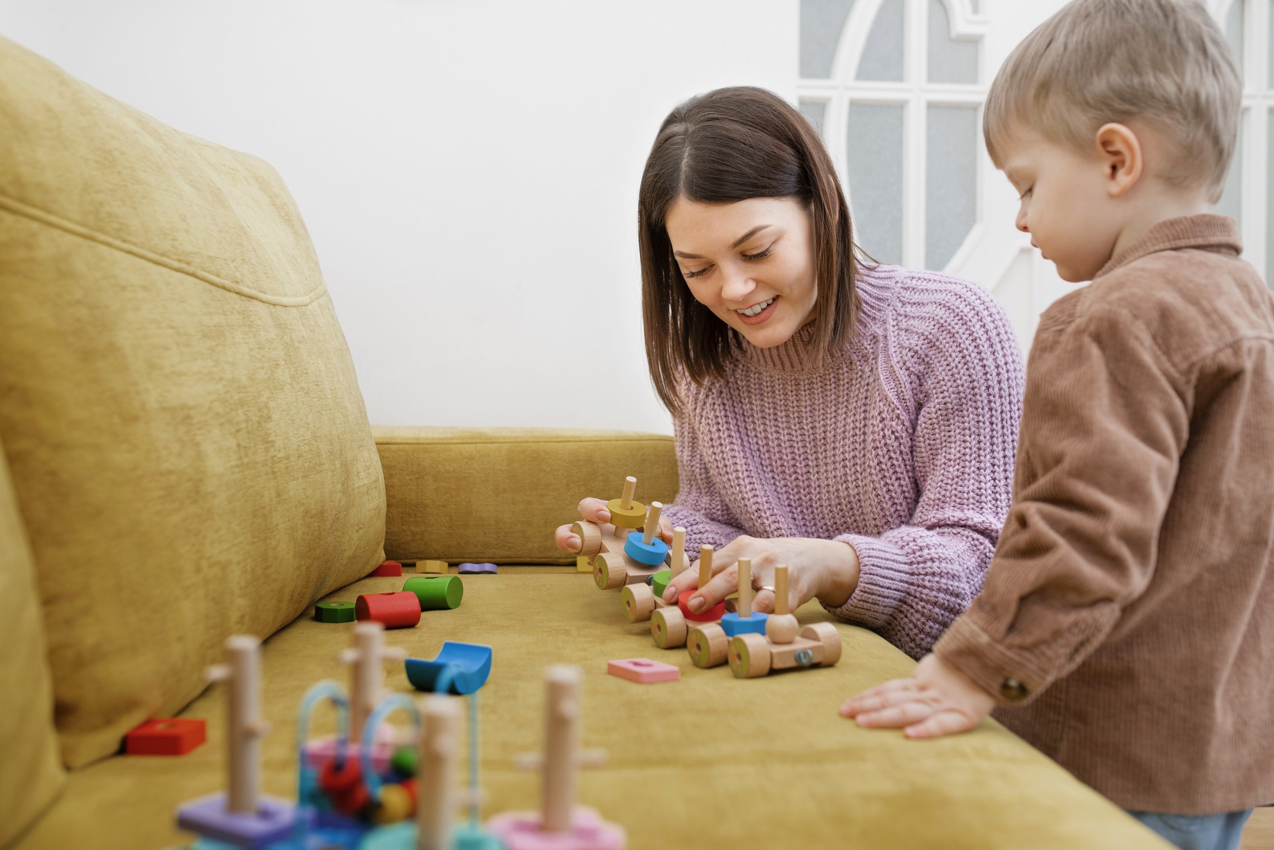 A woman and a young boy playing with wooden toys on a yellow sofa.