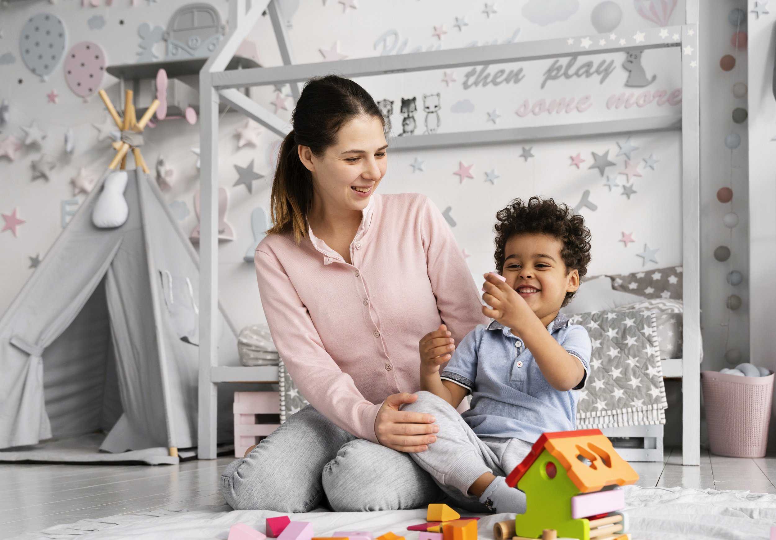 A woman and a young boy sitting on the floor playing with colorful wooden toys in a decorated children's bedroom.