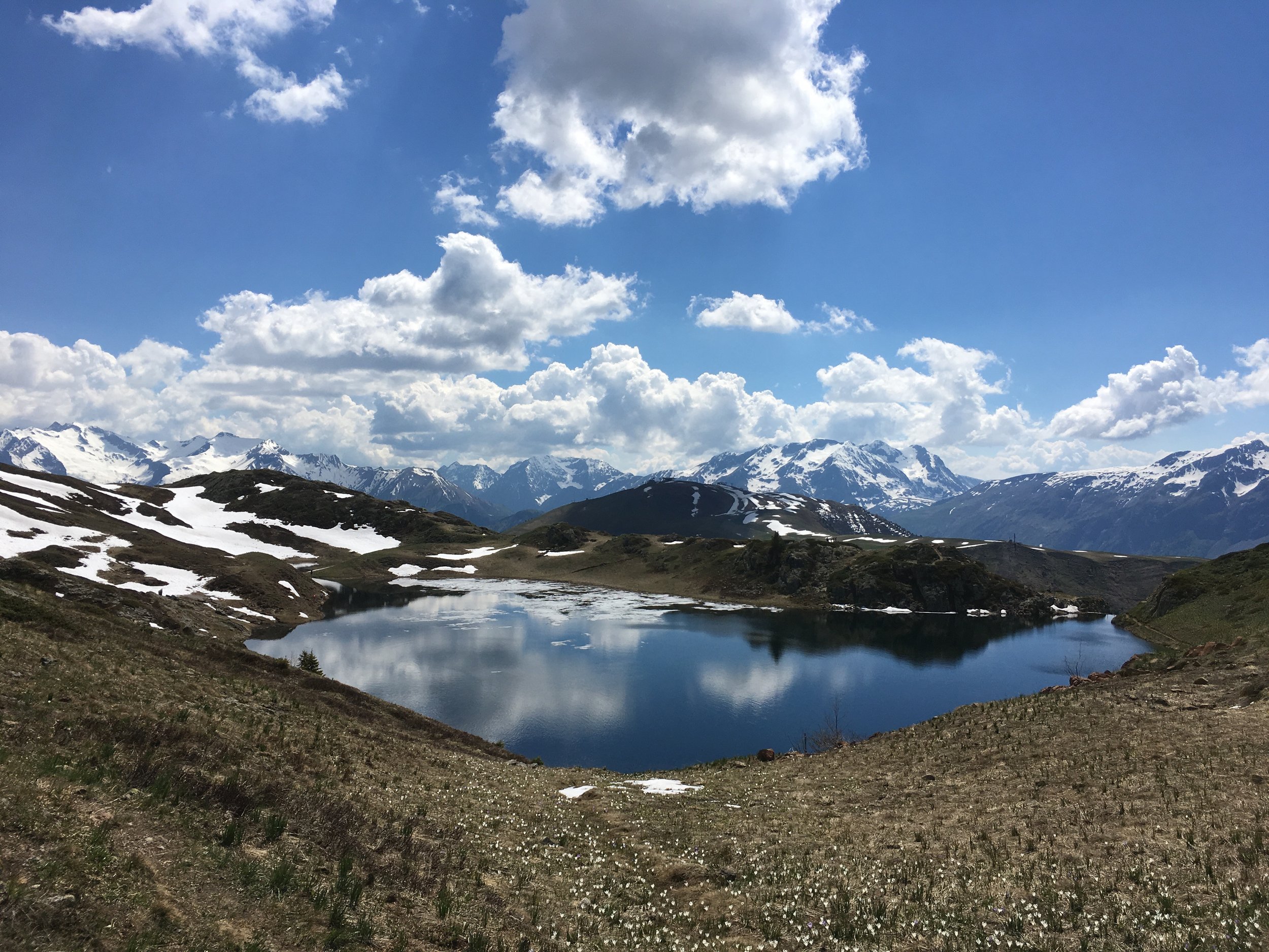 Montagnes enneigées avec un lac au premier plan, nuages dans le ciel bleu.