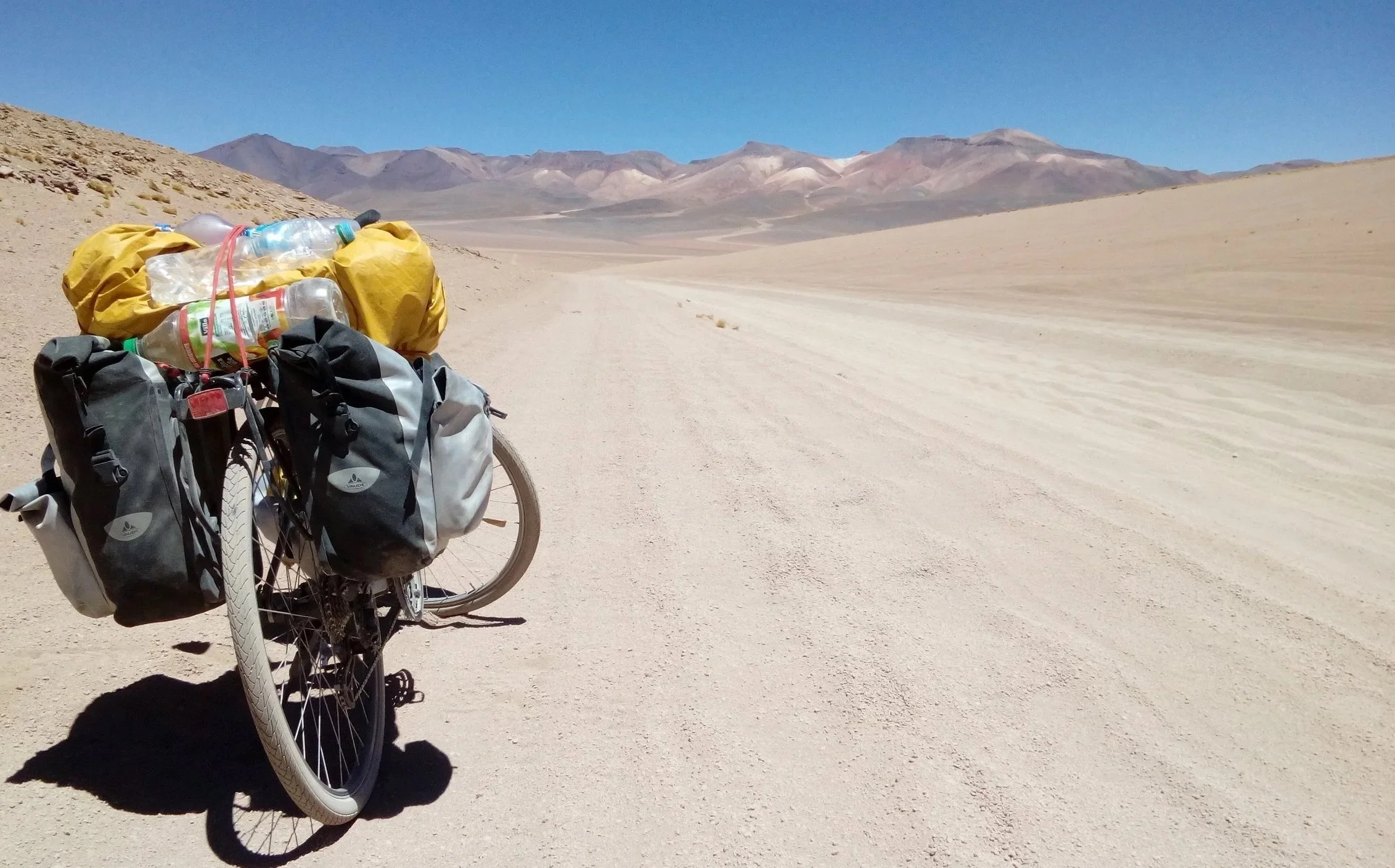 Photo d'un de mes voyage de mon vélo chargé de sacs dans un désert avec montagnes en arrière-plan. Pour montrer aussi mon expérience