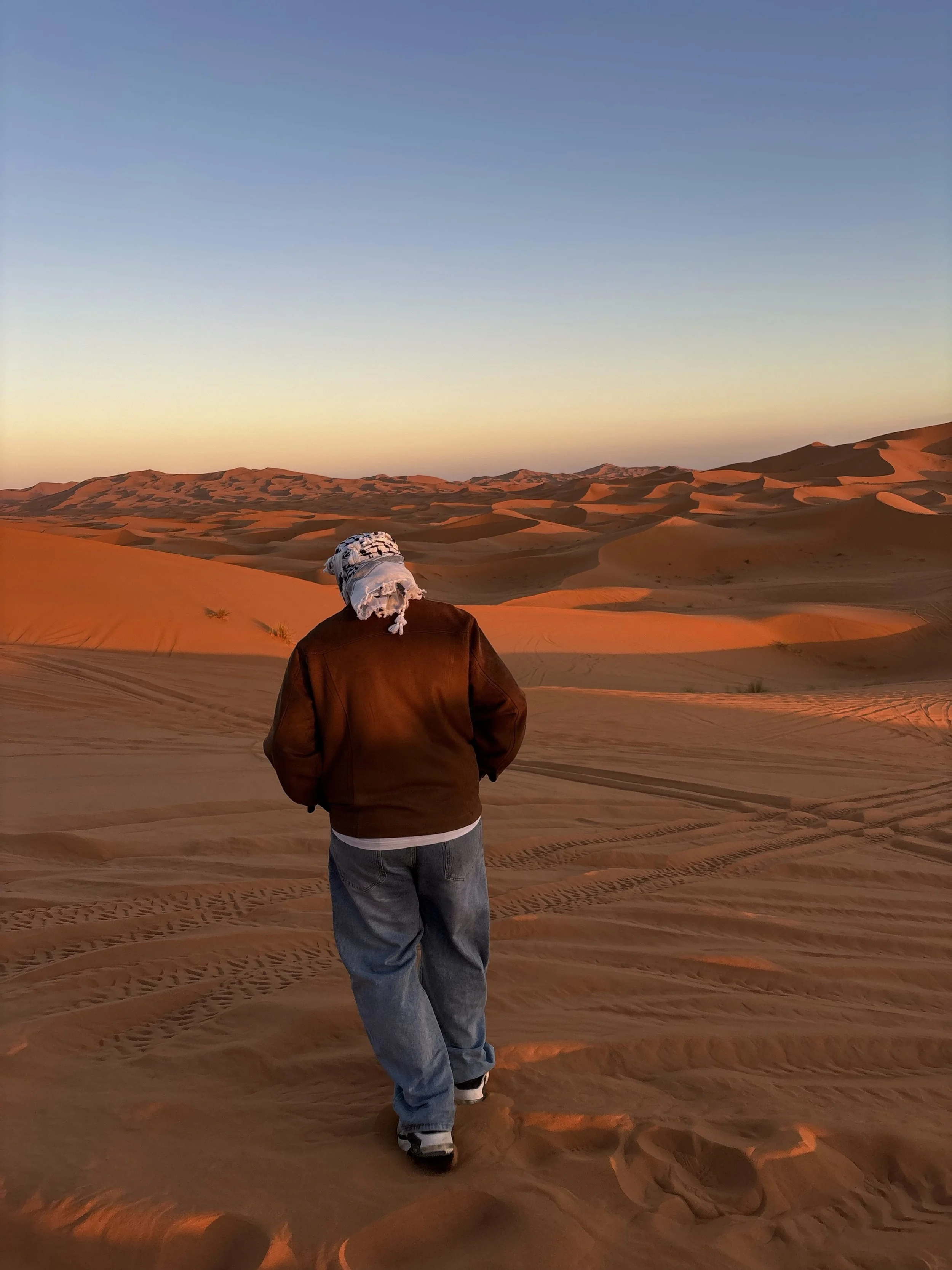 A person walking in a desert with sand dunes during sunset.