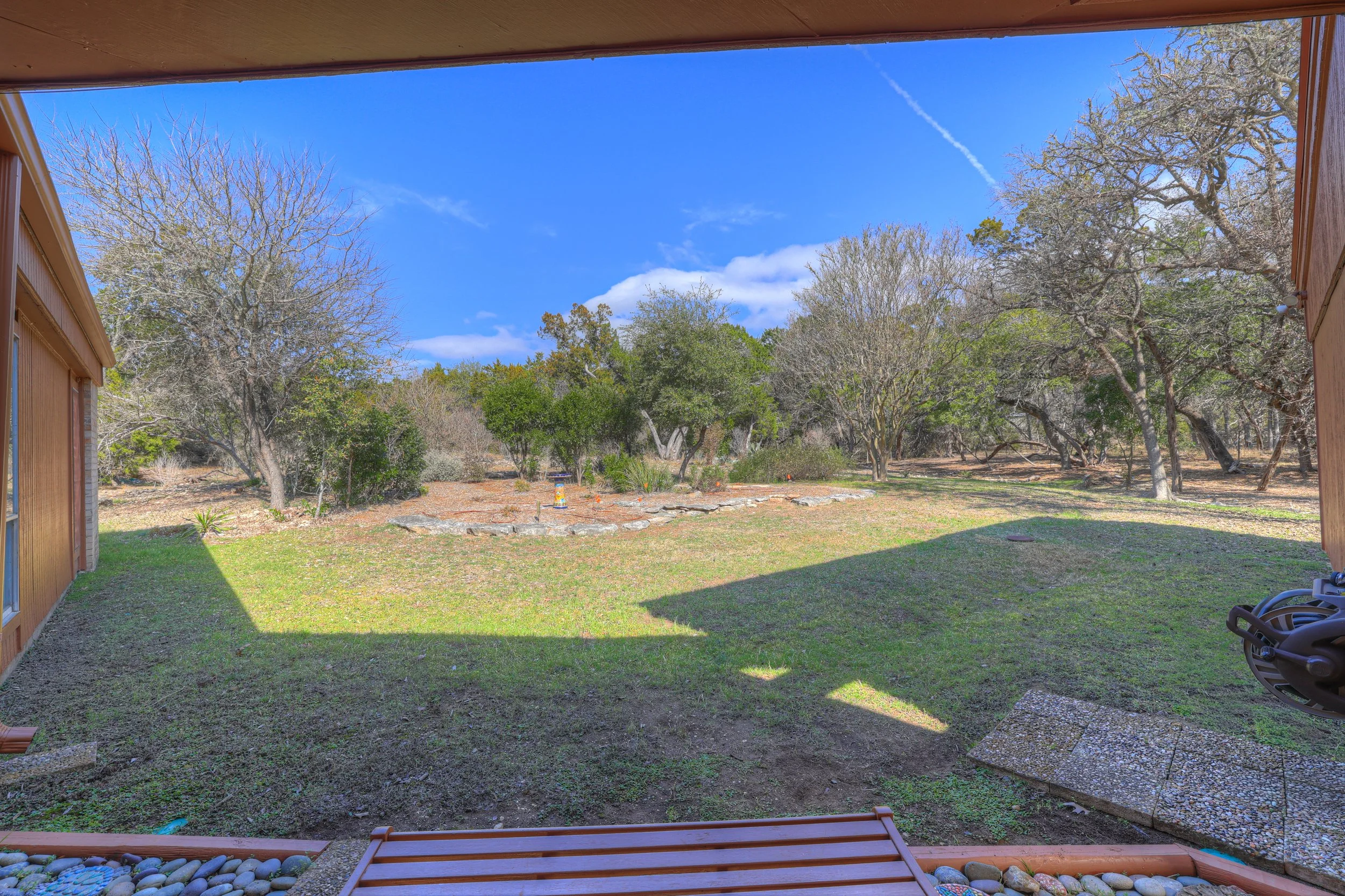 View of backyard with grass, trees, and sky, taken from porch or patio with wooden trim, rocks, and outdoor furniture