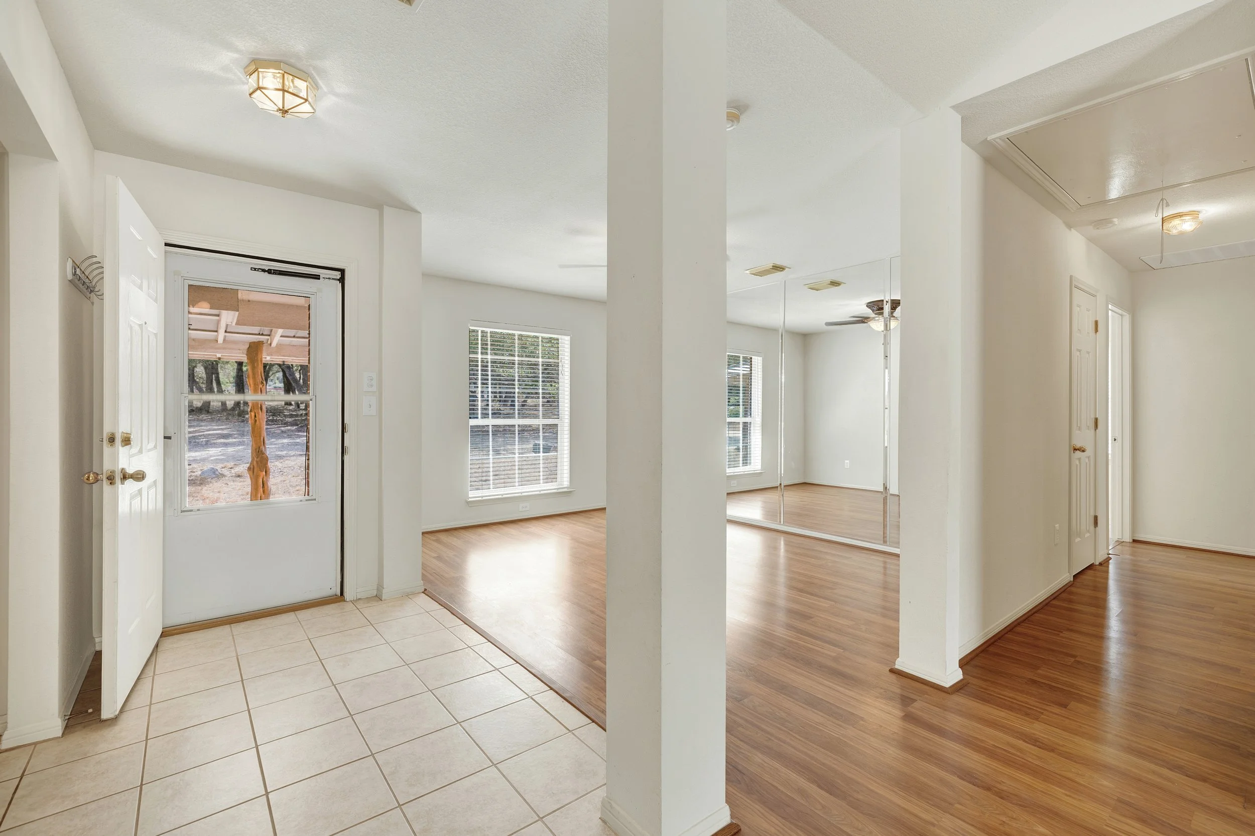 Empty interior of a house with tiled entryway, hardwood floors, a mirrored closet, and multiple windows allowing natural light.