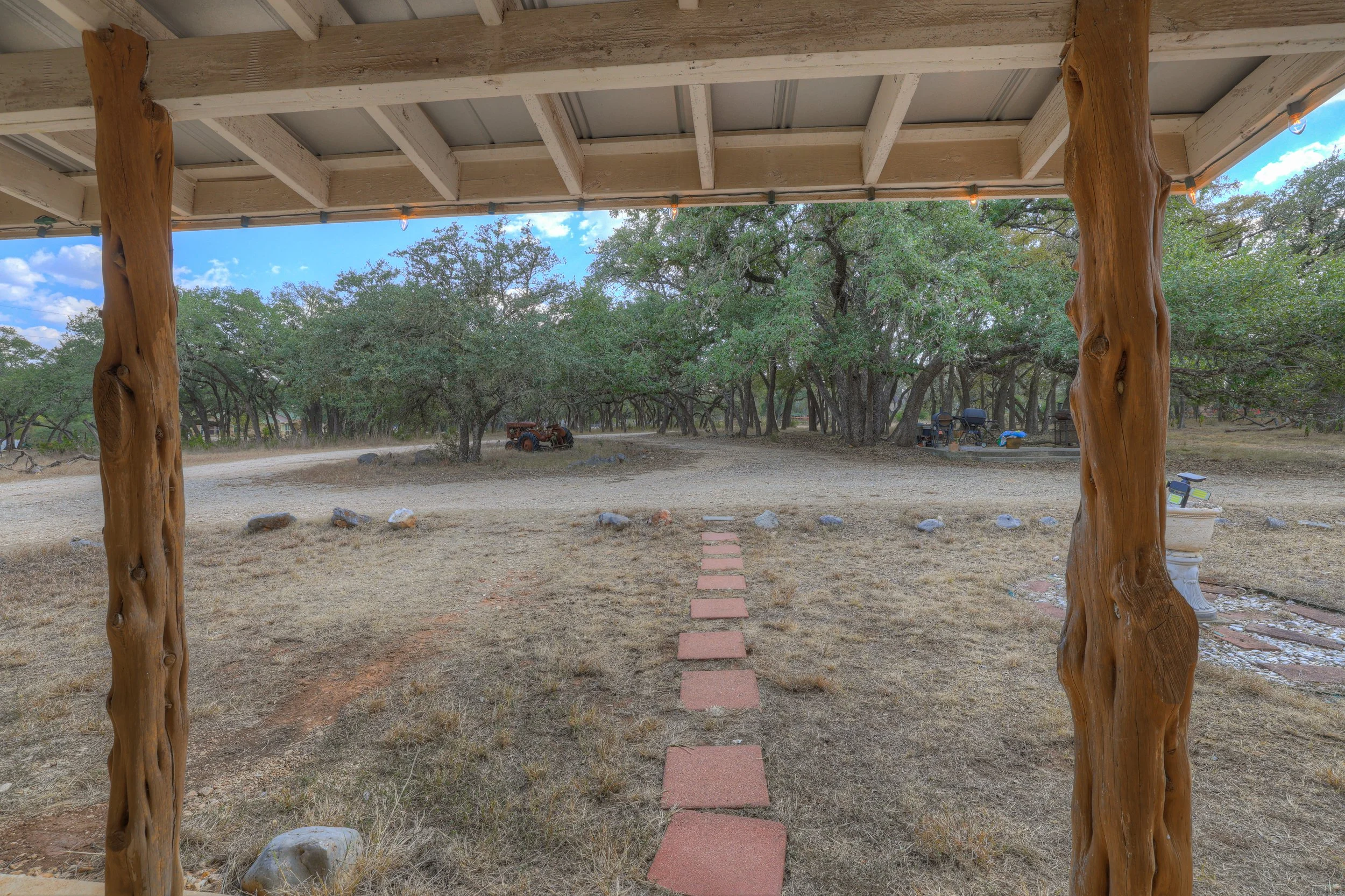 View from a covered porch of a yard with a pathway of red stepping stones, surrounded by trees and outdoor furniture.