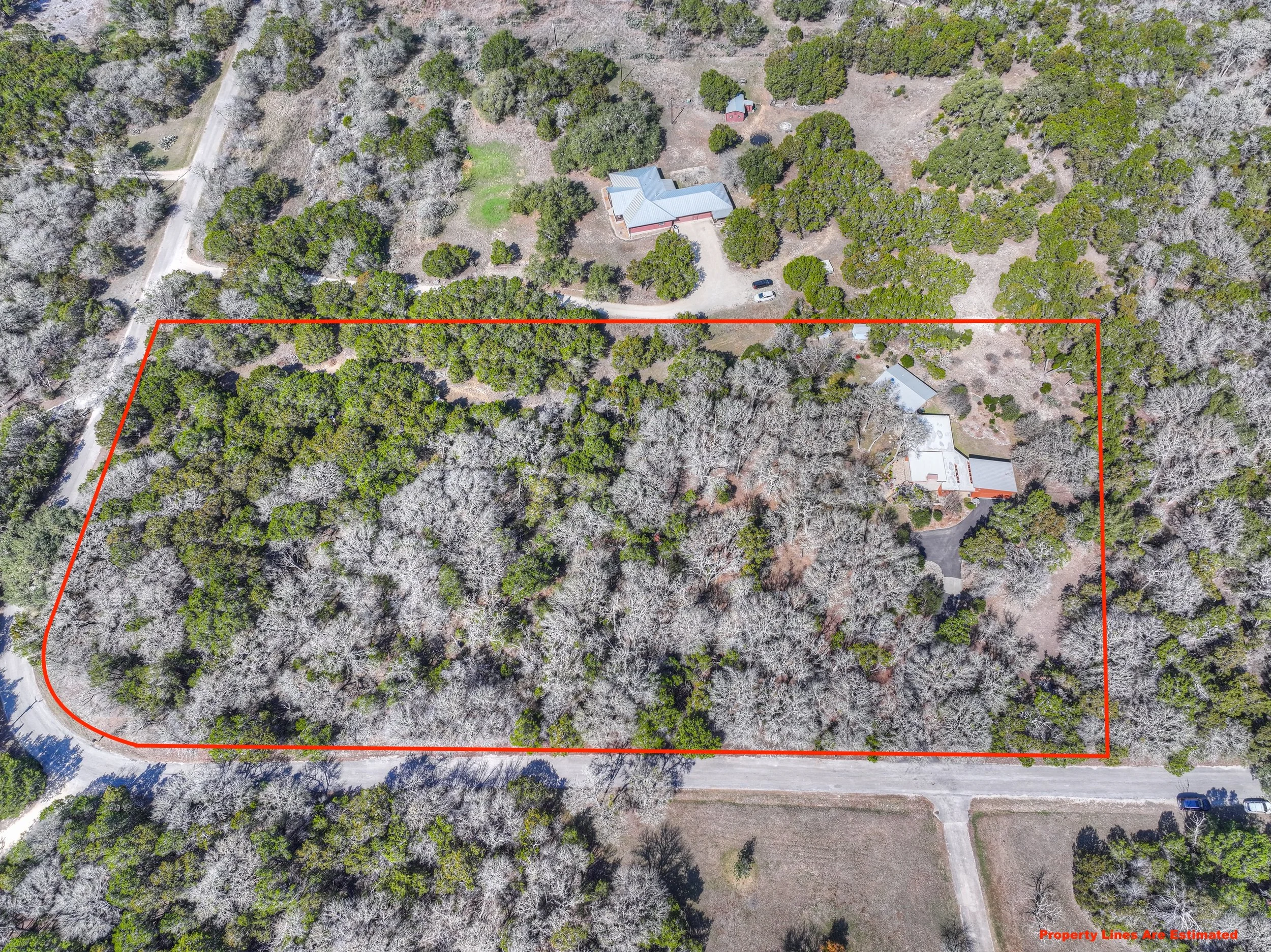 Aerial view of a wooded property outlined in red, with neighboring homes and roads visible.