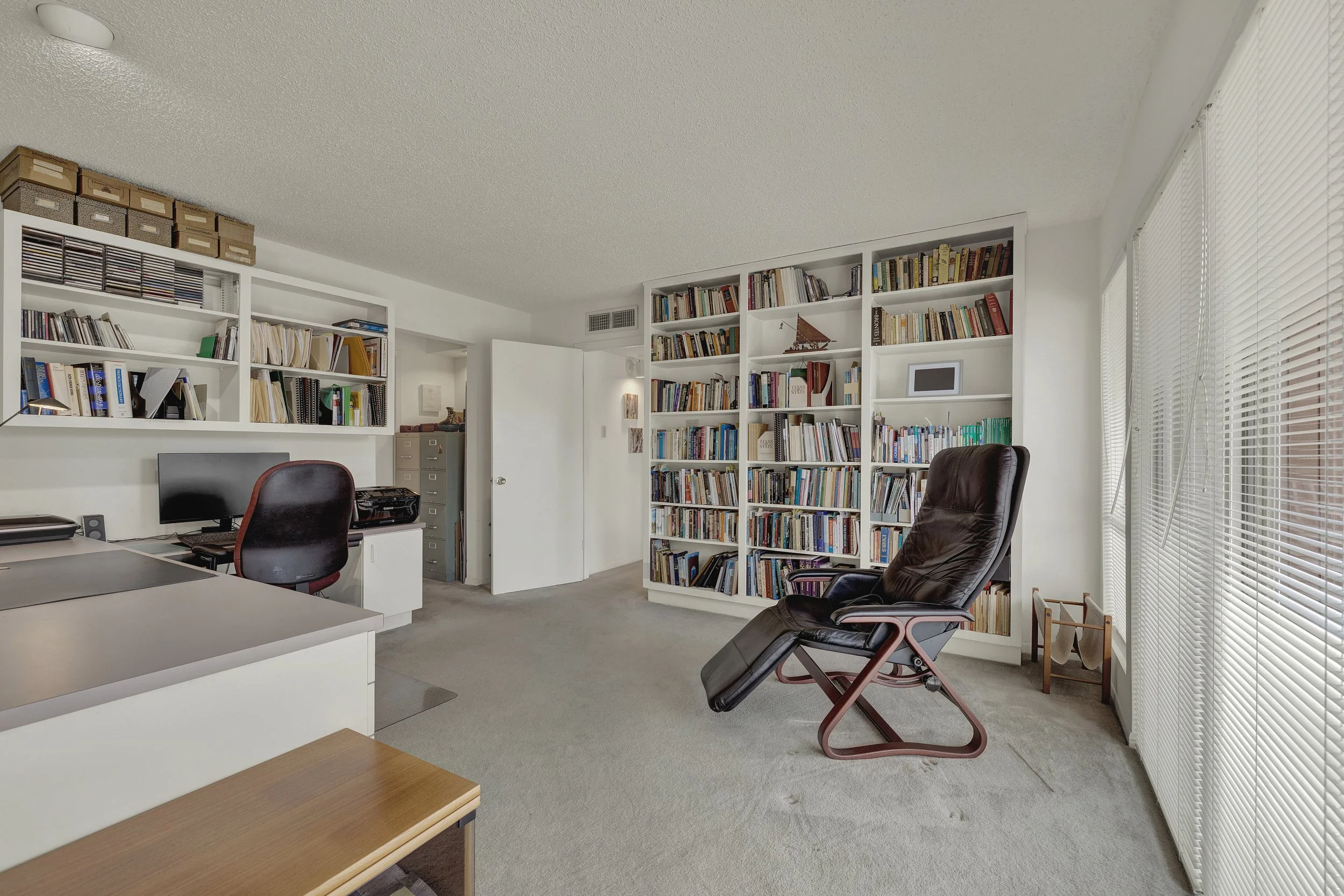 Home office with bookshelves, a computer desk, and a leather recliner near sliding glass doors.