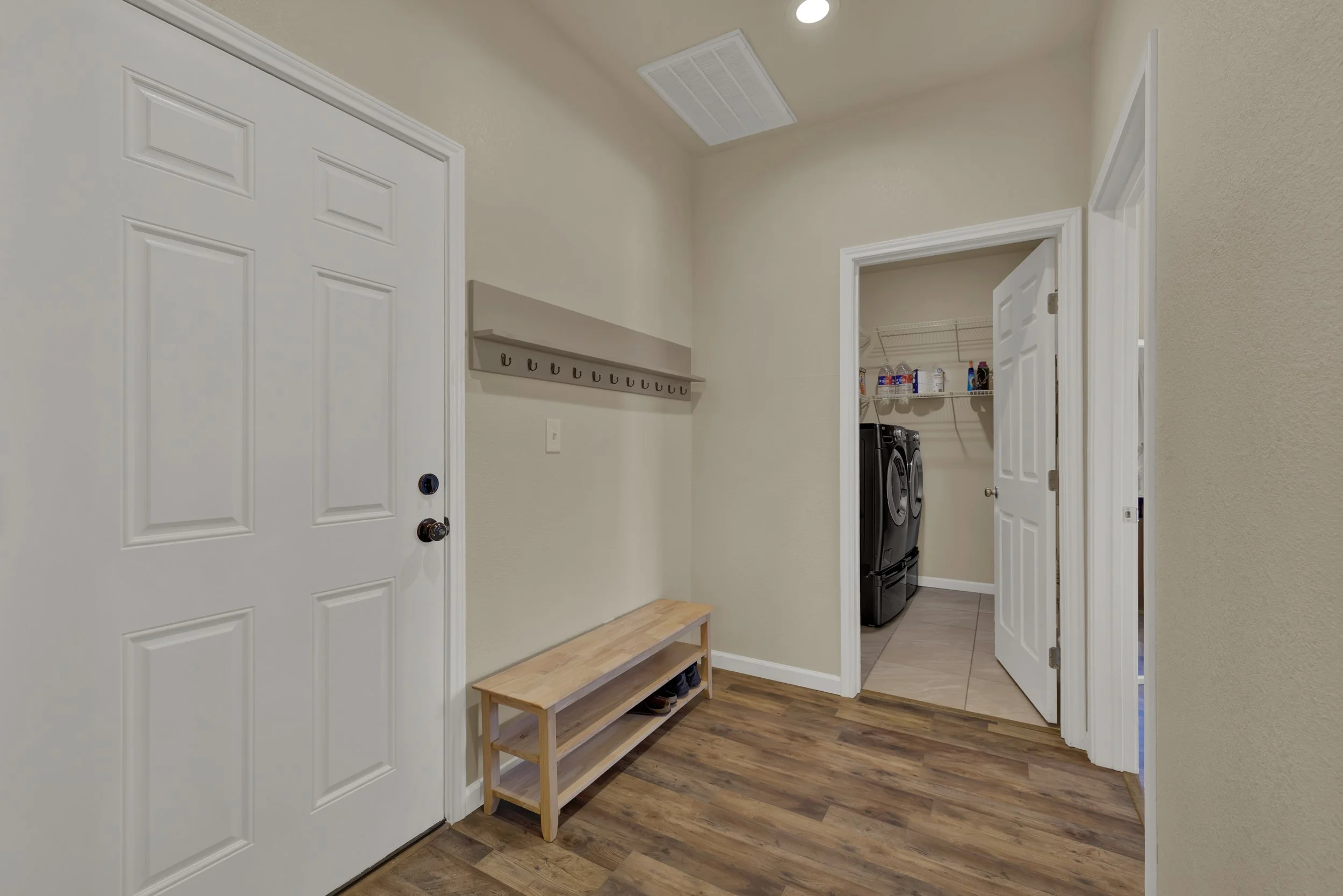 Entryway with a white door, a wooden bench, hook rack, beige walls, and a view into a laundry area with a washer and dryer.