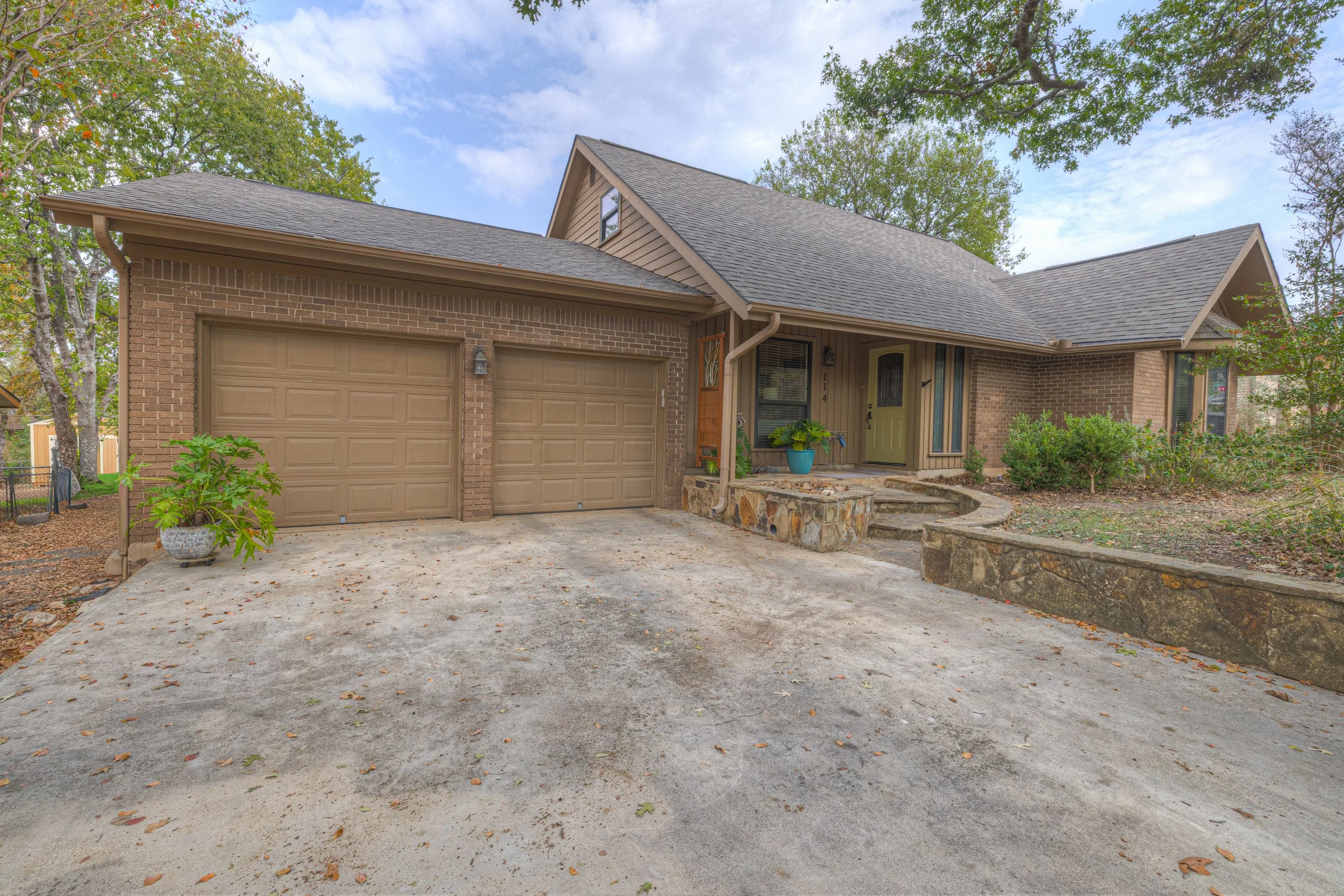 Front view of a house with a two-car garage, stone steps leading to a front porch, and surrounded by trees and bushes.