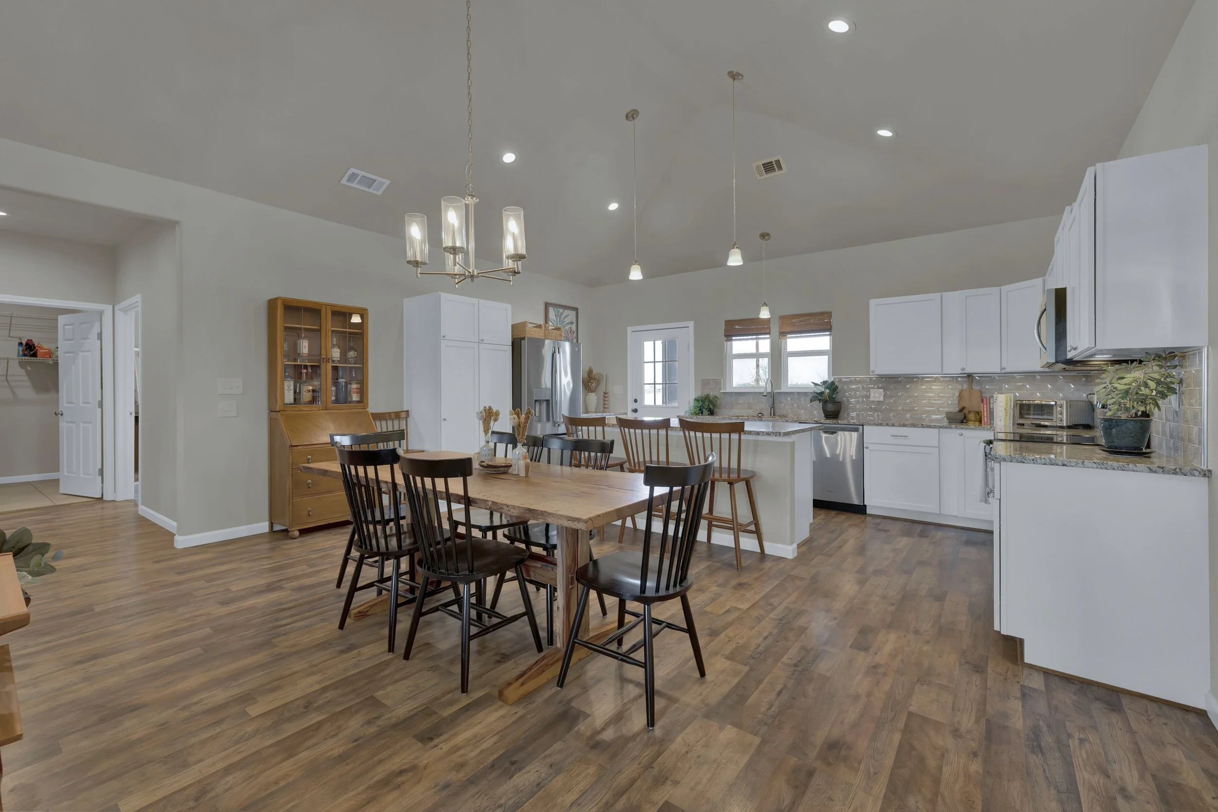 Open concept kitchen and dining area with white cabinets, wooden dining table, black chairs, and hardwood flooring.